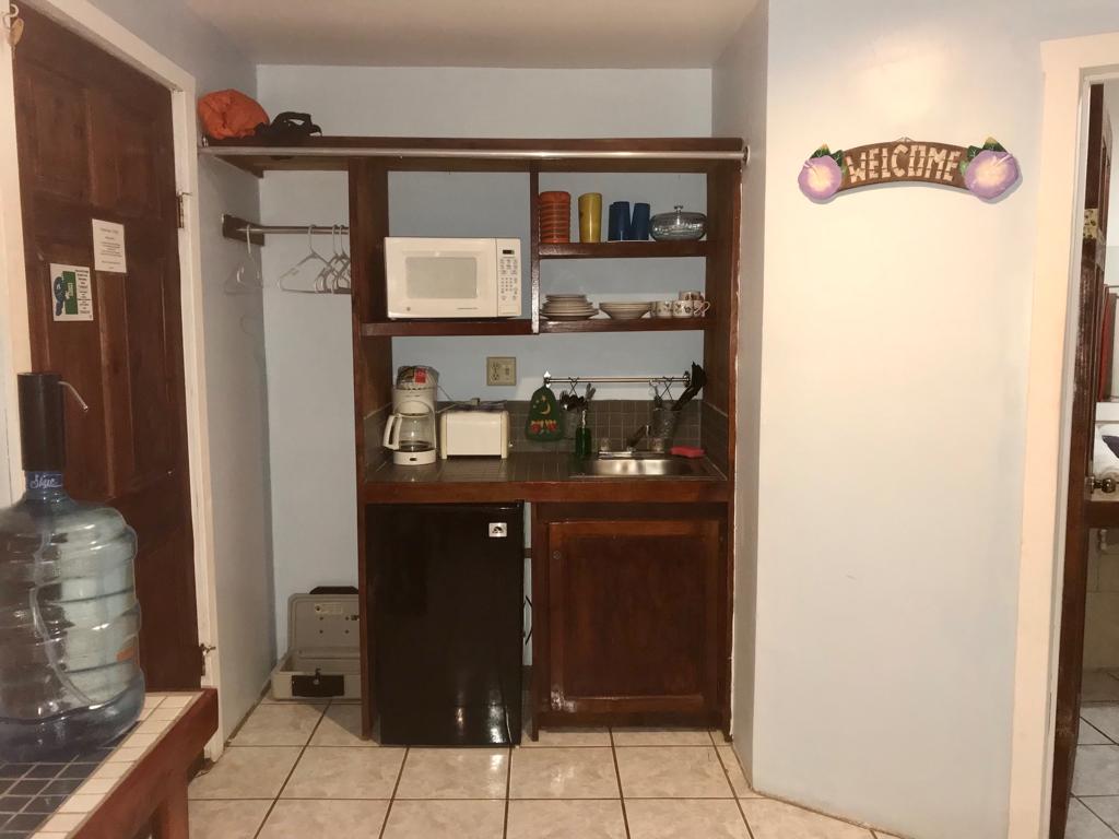 Small kitchen with a microwave, mini-fridge, and shelves with food, in a room with a 