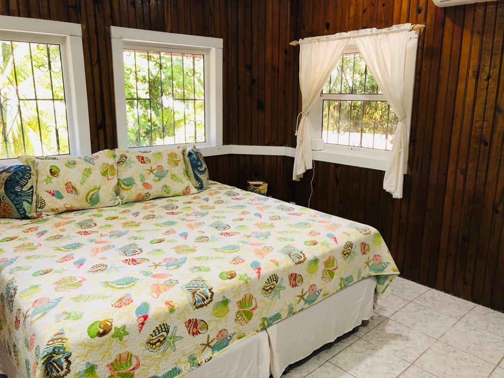 Bedroom with wood-paneled walls, a bed covered in a seashell-patterned quilt, and three windows with natural light.