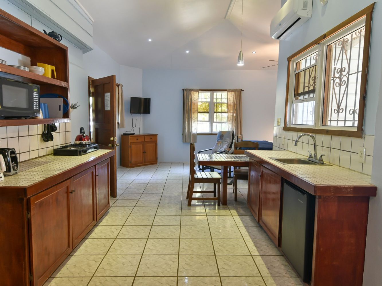 Kitchen and living area in a tropical-style rental home with tile floors, wood cabinets, and a dining table.