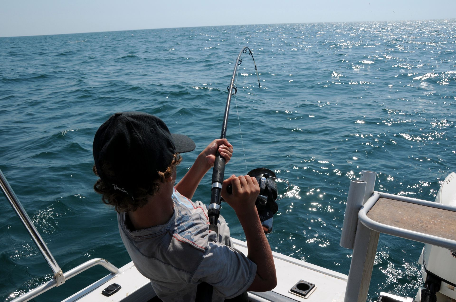 A person fishing from a boat on a sunny day, pulling on a bent fishing rod.