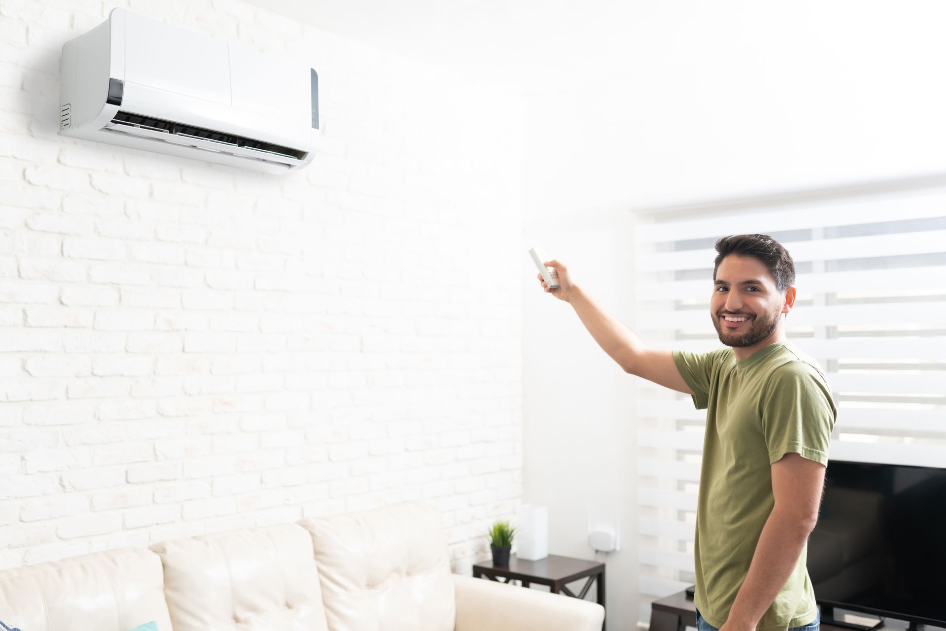 Smiling man using a remote to control a wall-mounted mini-split AC unit in a modern living room.