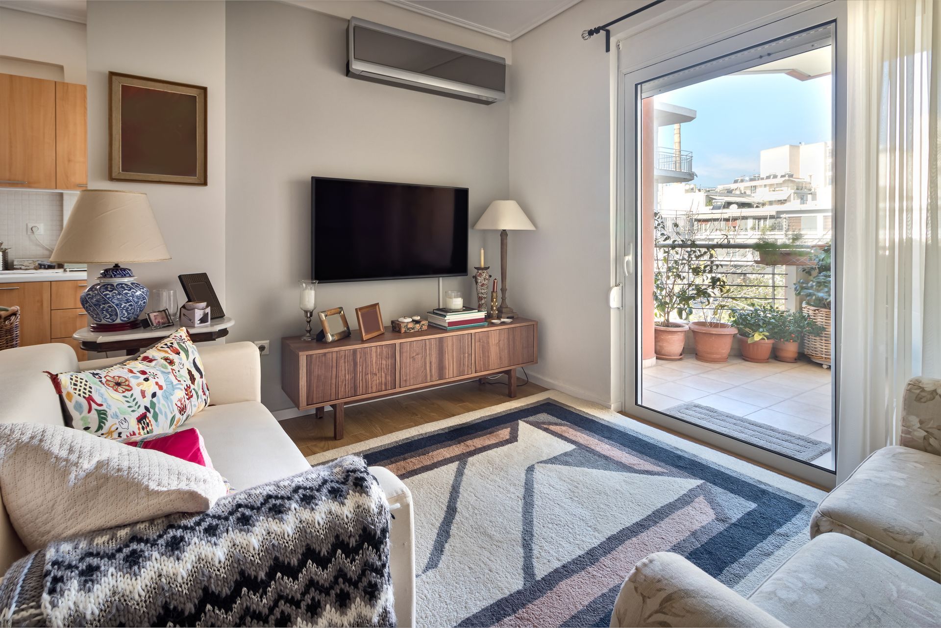 Wall-mounted mini-split AC in a cozy living room with TV, sofa, and balcony view.