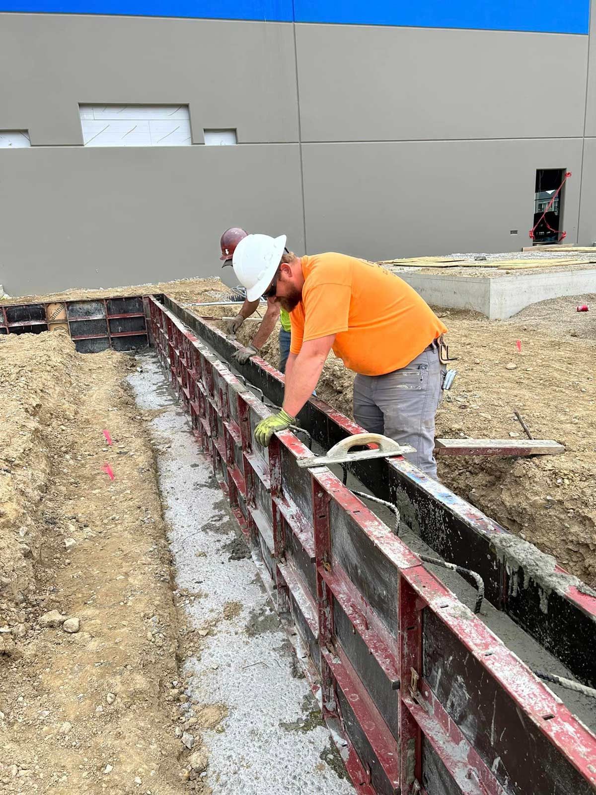 A Man In An Orange Shirt Is Working On A Concrete Wall — Chesterton, IN — Claycor Construction