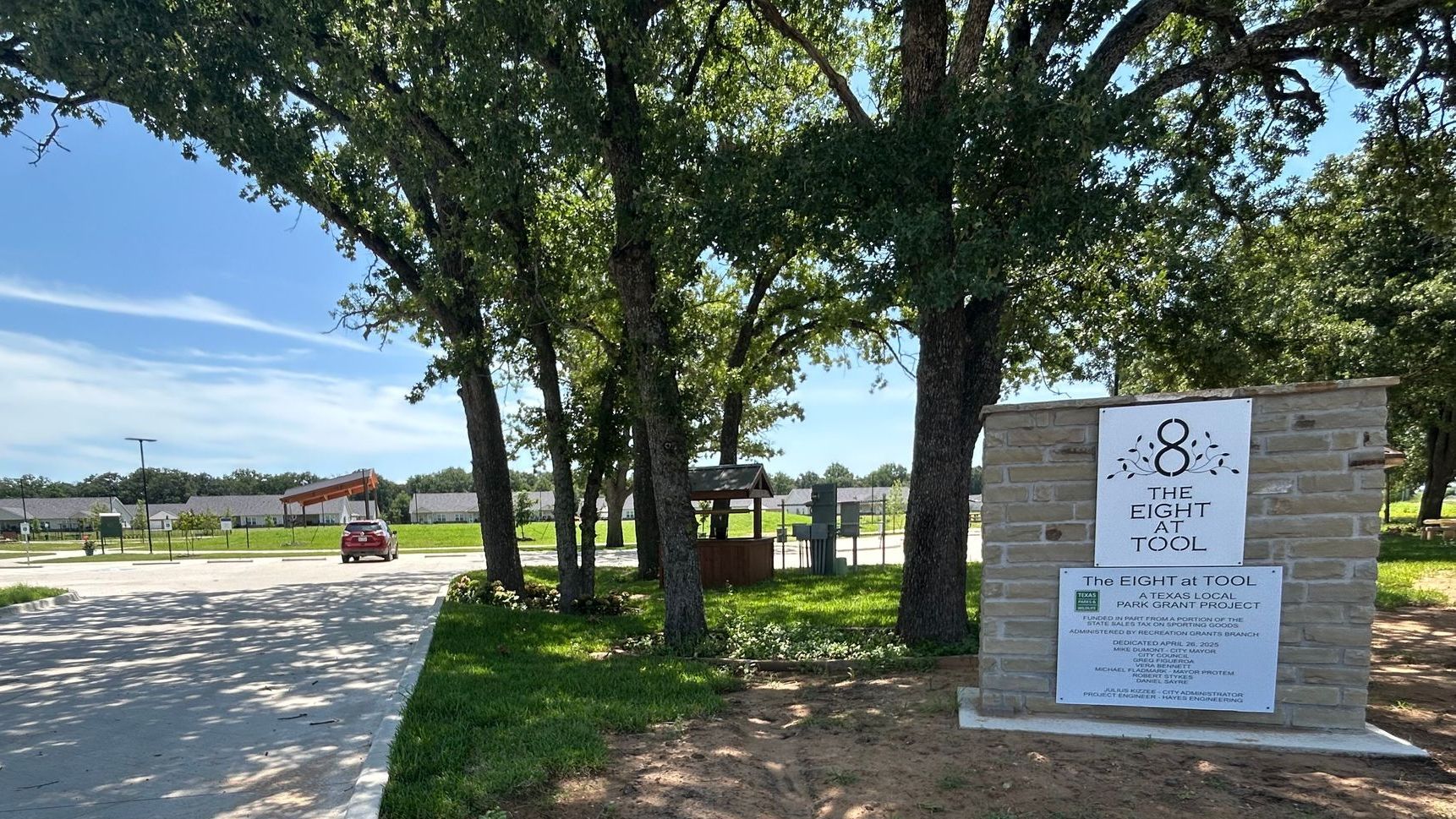 A brick wall with a sign on it is surrounded by trees and grass.