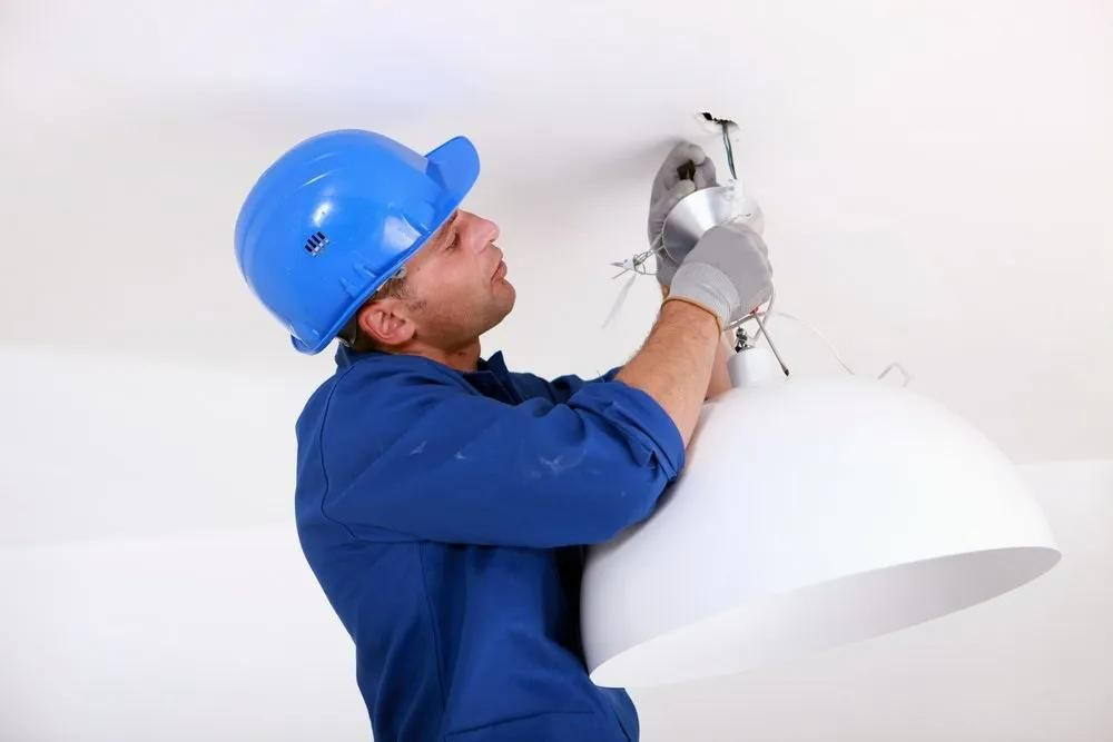 A Man is Installing a Light Fixture on the Ceiling — Clifford Electrical in Ballina, NSW