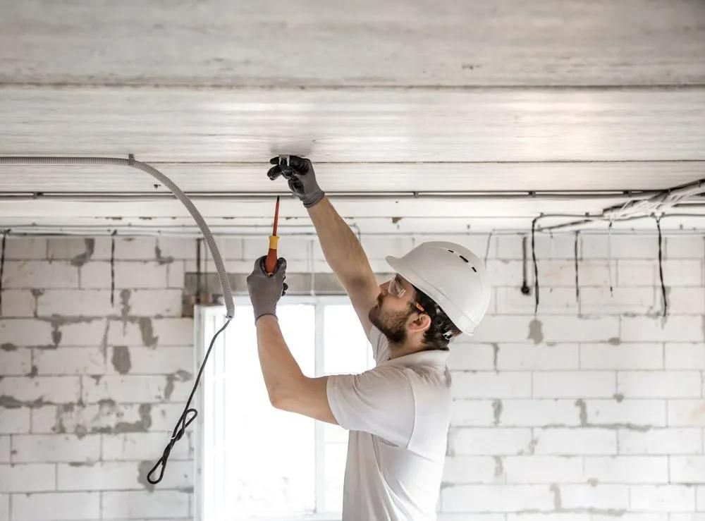 A Man is Working on a Ceiling With a Screwdriver — Clifford Electrical in Alstonville, NSW