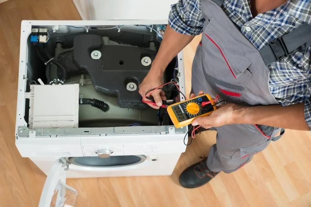 A Man is Fixing a Washing Machine With a Multimeter — Clifford Electrical in Ballina, NSW