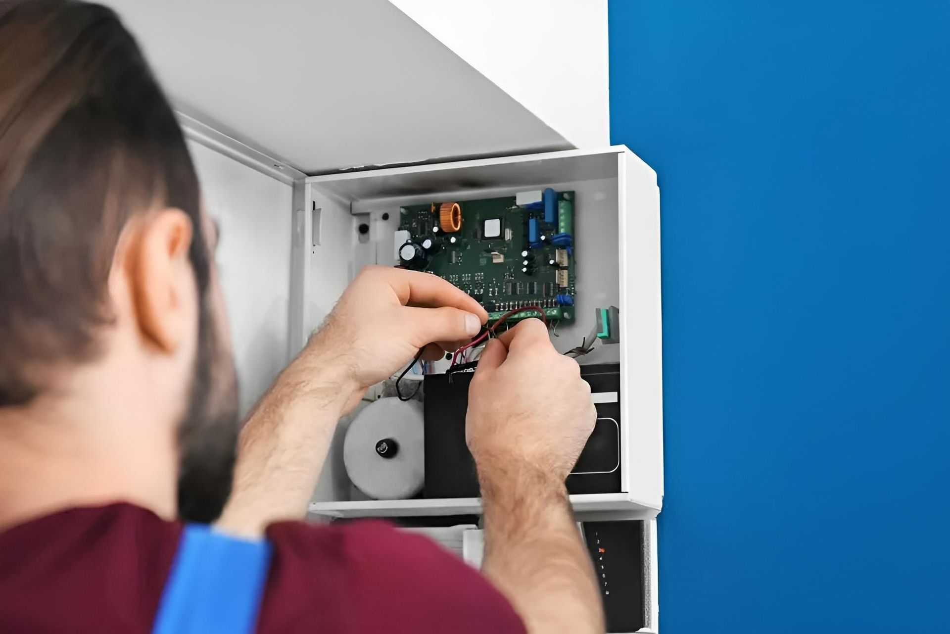 A Man is Fixing a Security System With a Screwdriver — Clifford Electrical in Ballina, NSW
