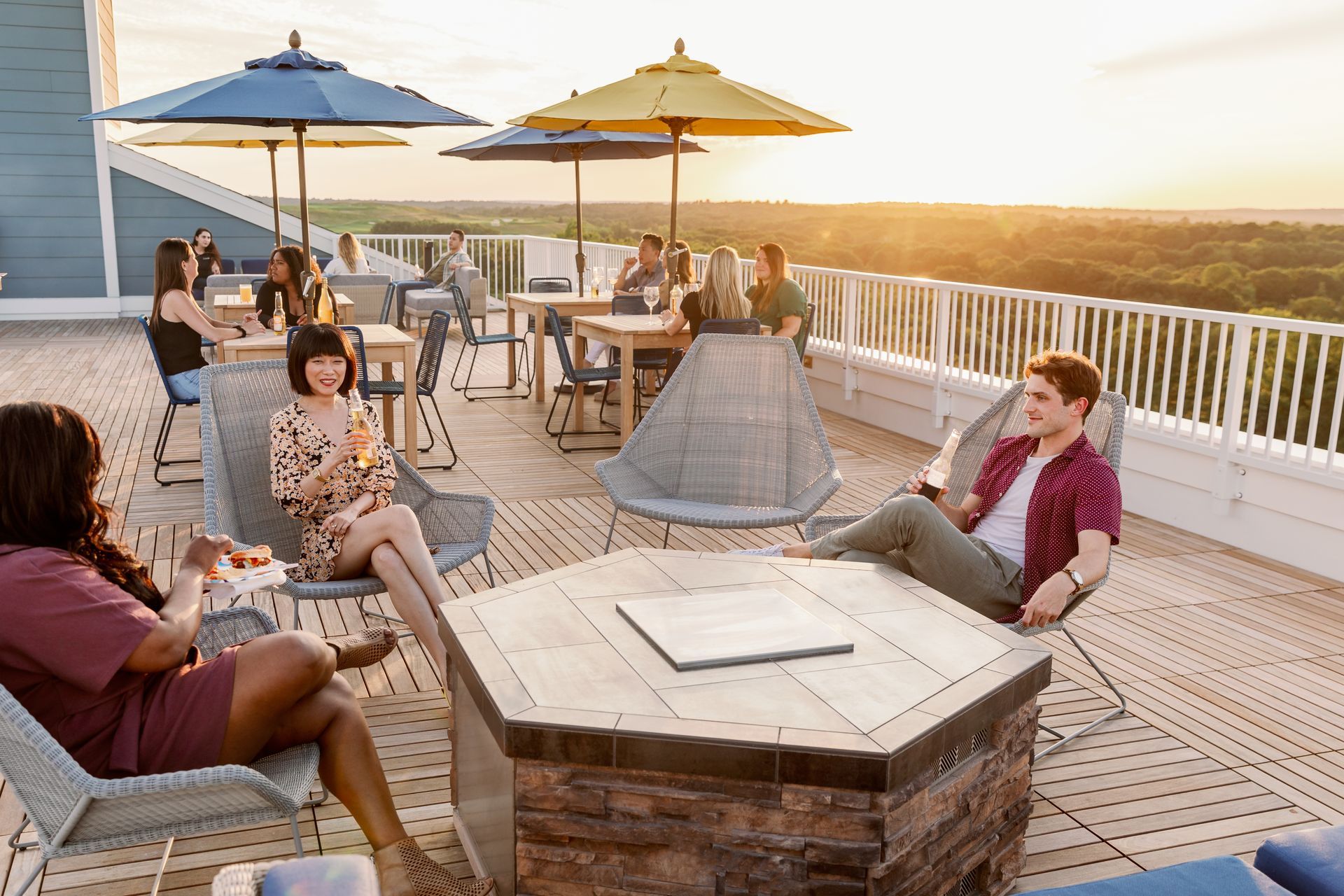 A group of people sitting around the fire pit on the rooftop lounge with beautiful sunset. 