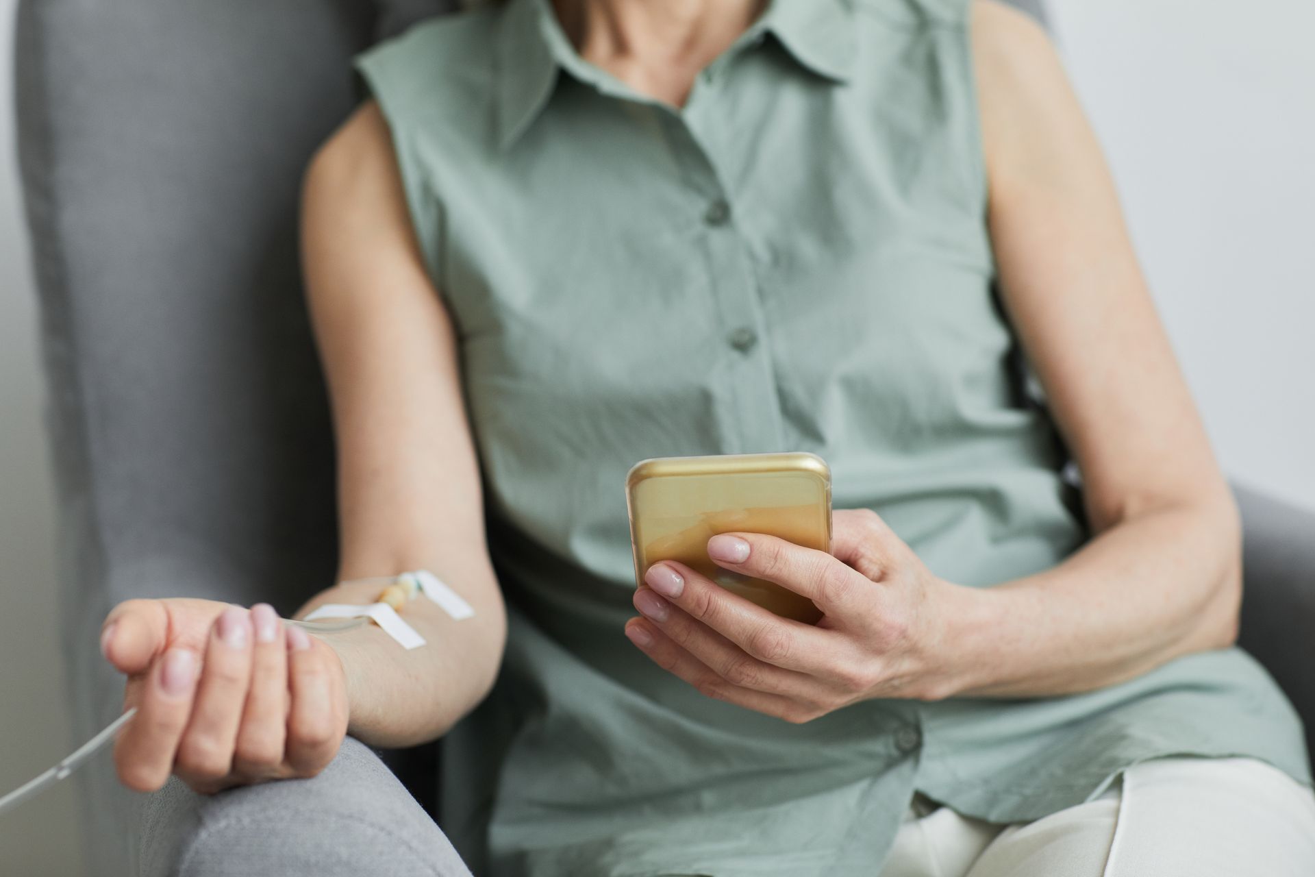 A woman is sitting in a chair holding a cell phone and a syringe in her arm.