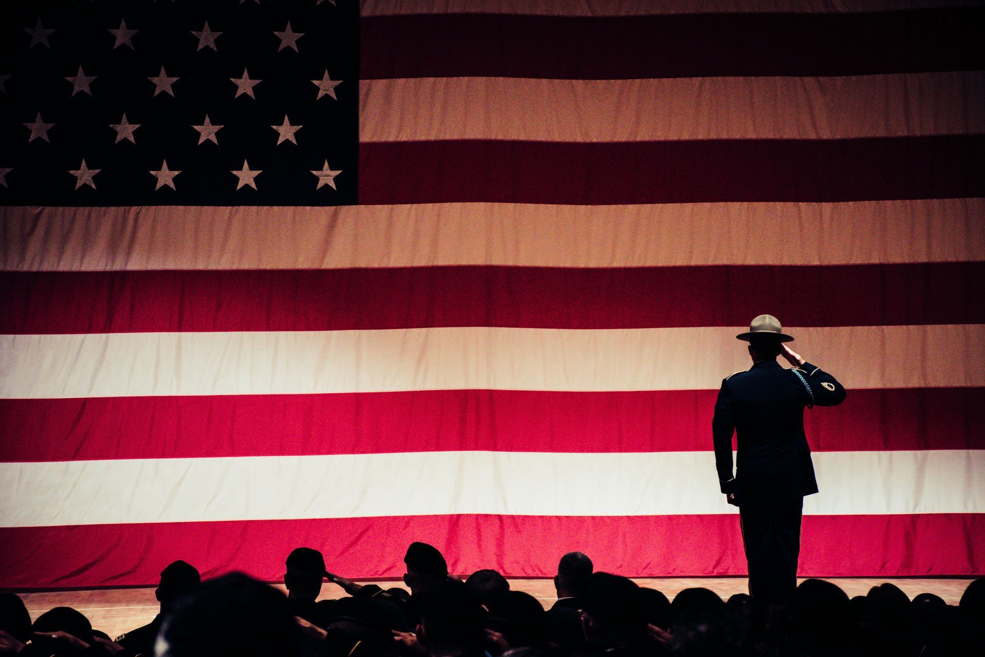 A man in a hat is saluting in front of an american flag.