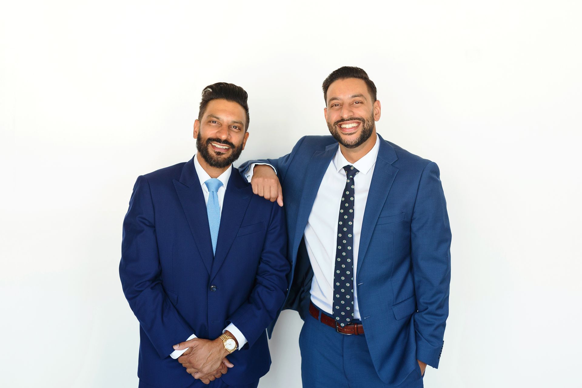 Two men in suits smile, one with arm on other's shoulder, against white background.