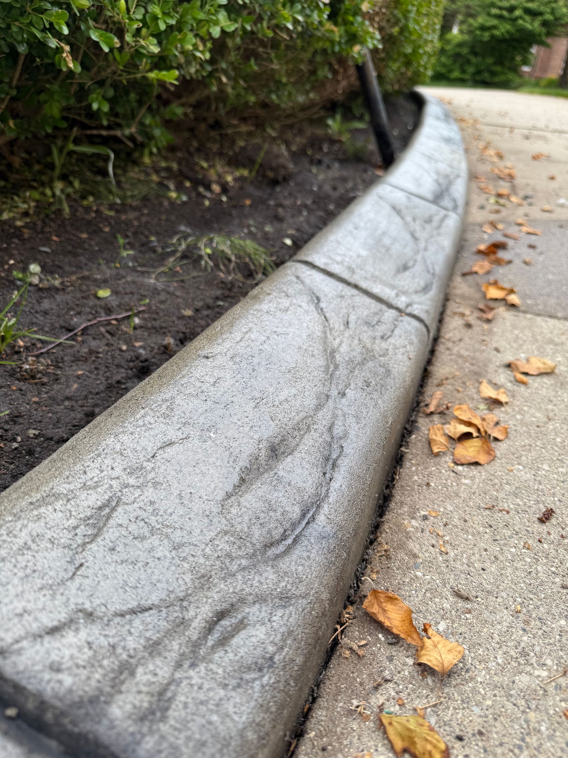 A blue car is parked in front of a house next to a flower bed.