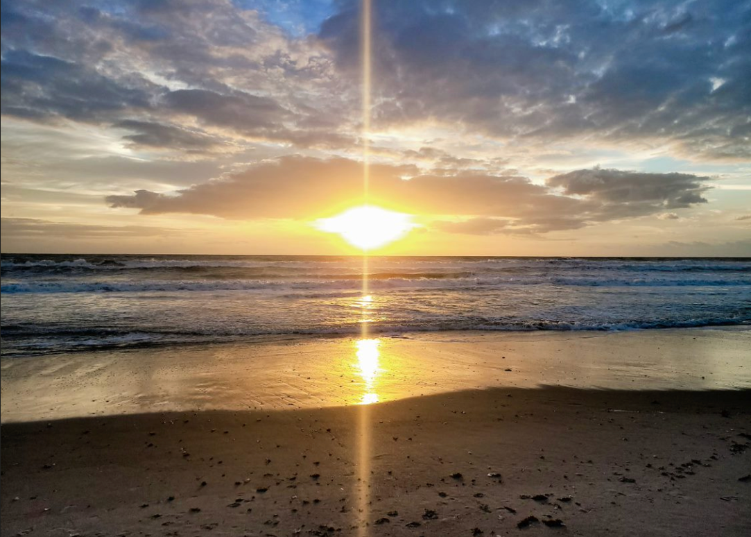 The sun is setting over the ocean on a cloudy day