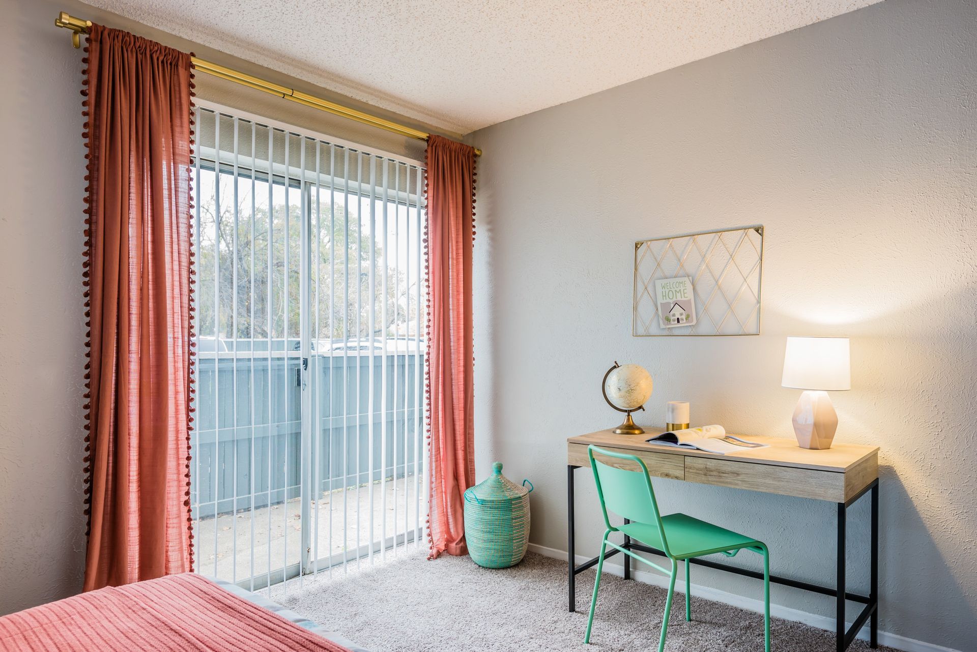 Bedroom with desk, pink curtains, sliding glass door, and a green chair.