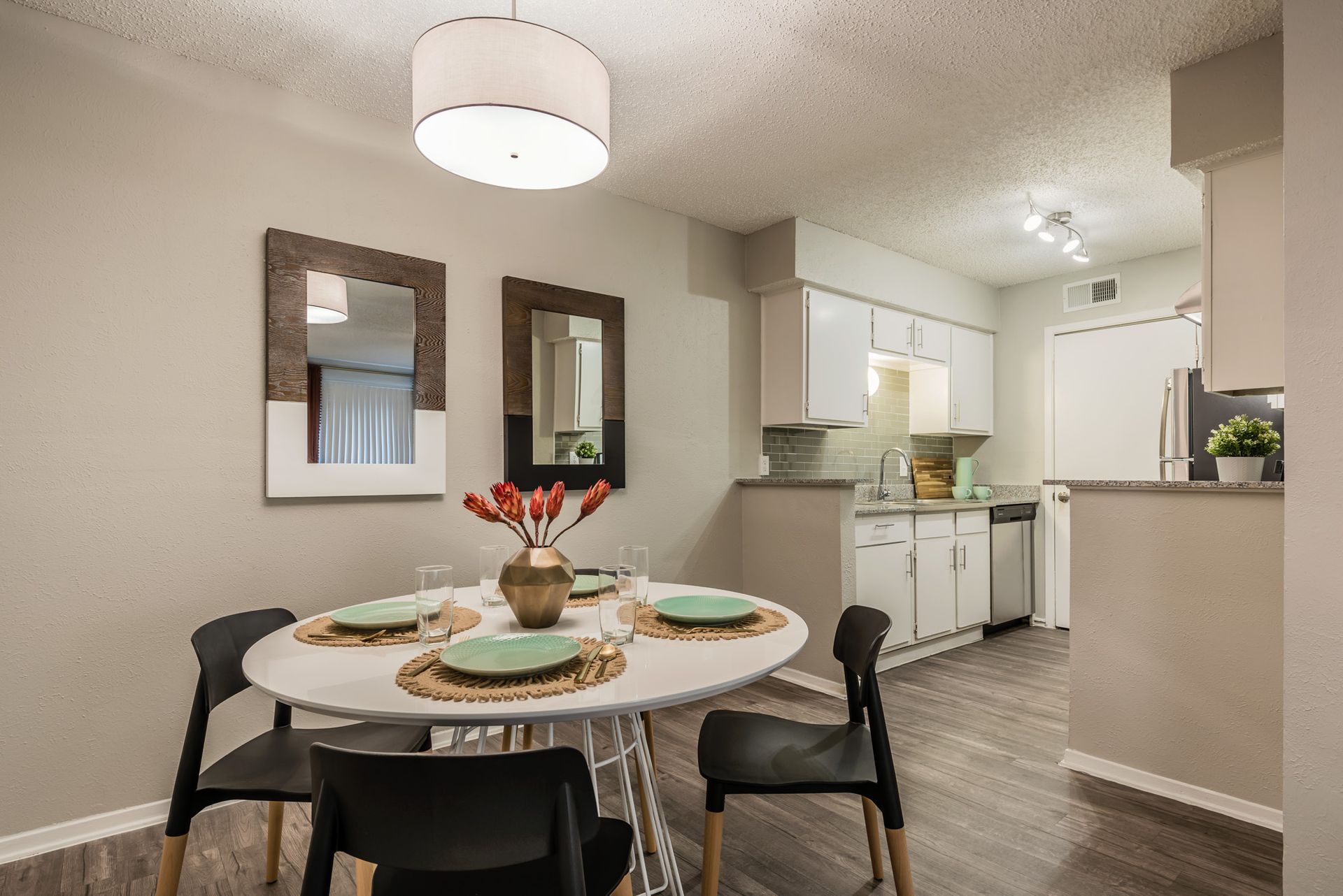Dining room with round white table, four black chairs, two mirrors, and a doorway to a kitchen.