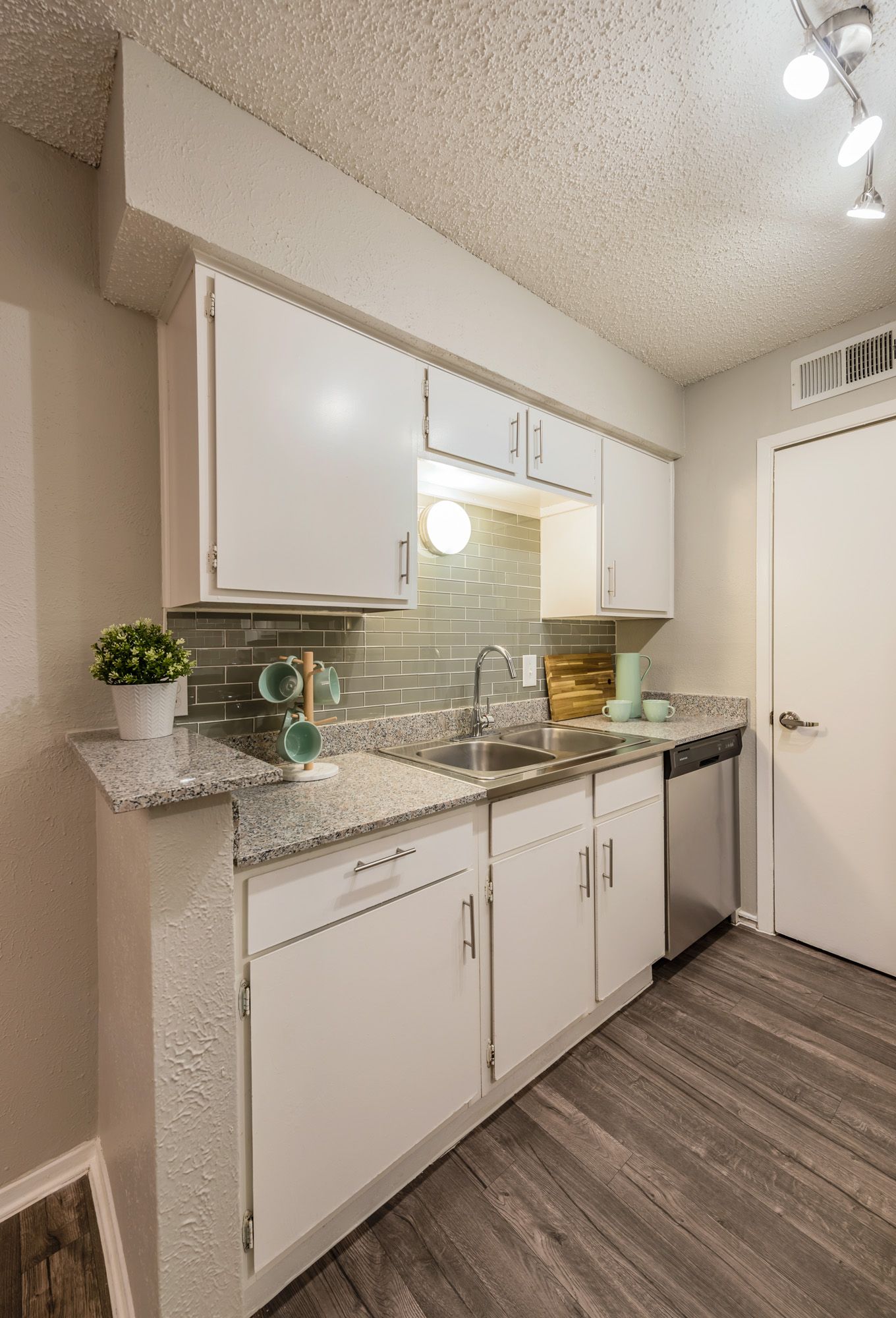 White kitchen with gray countertops, stainless steel appliances, and wooden floors.