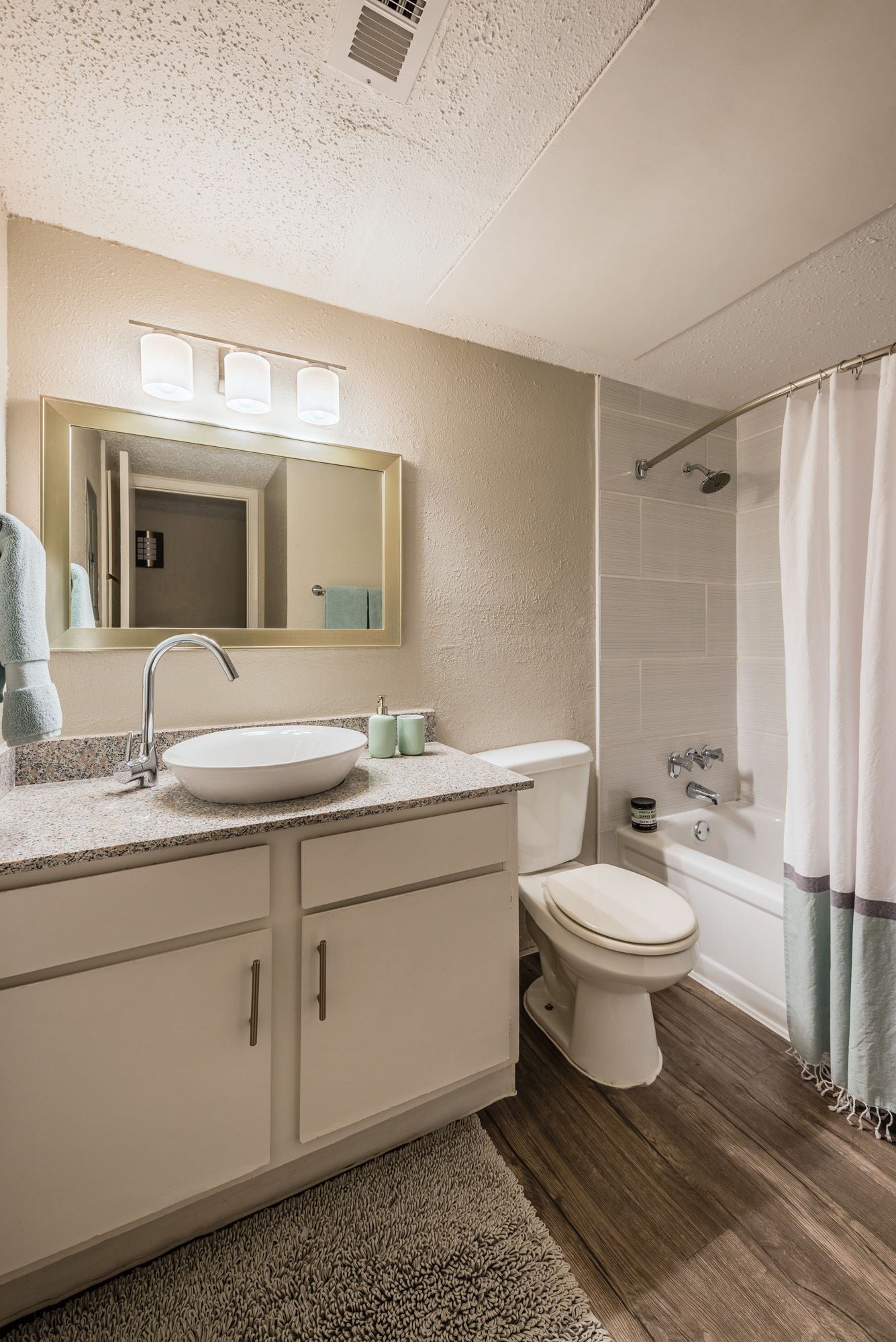 Bathroom with white vanity, toilet, and shower/tub.  Mirror, lighting, and light blue accents.