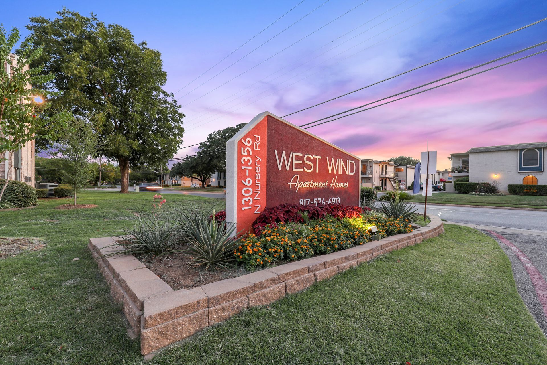 West Wind Apartments sign at dusk with landscaping and street view.