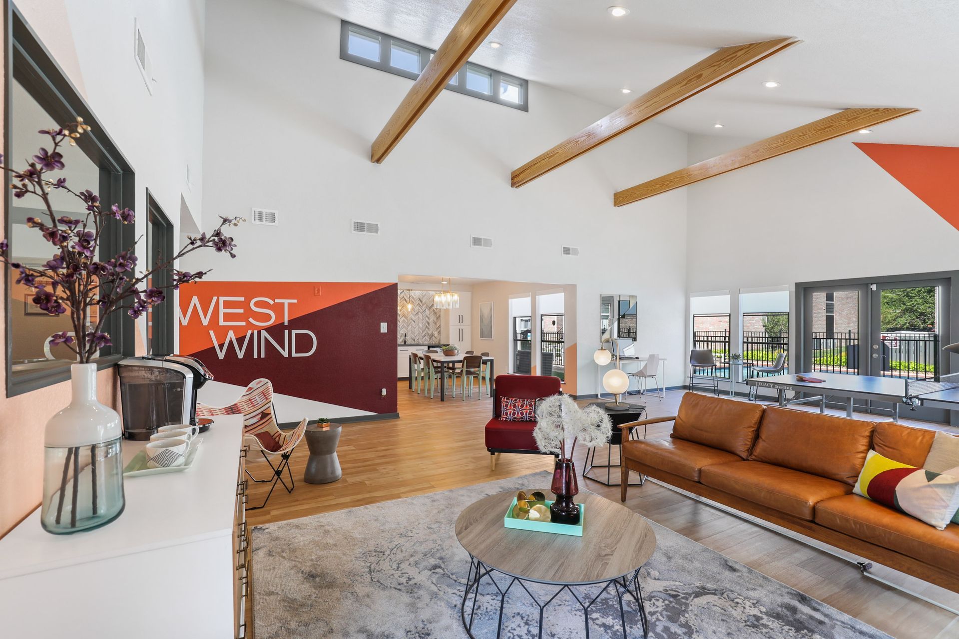 Bright, modern West Wind apartment lobby with orange and red accents, leather couch, and vaulted ceiling.