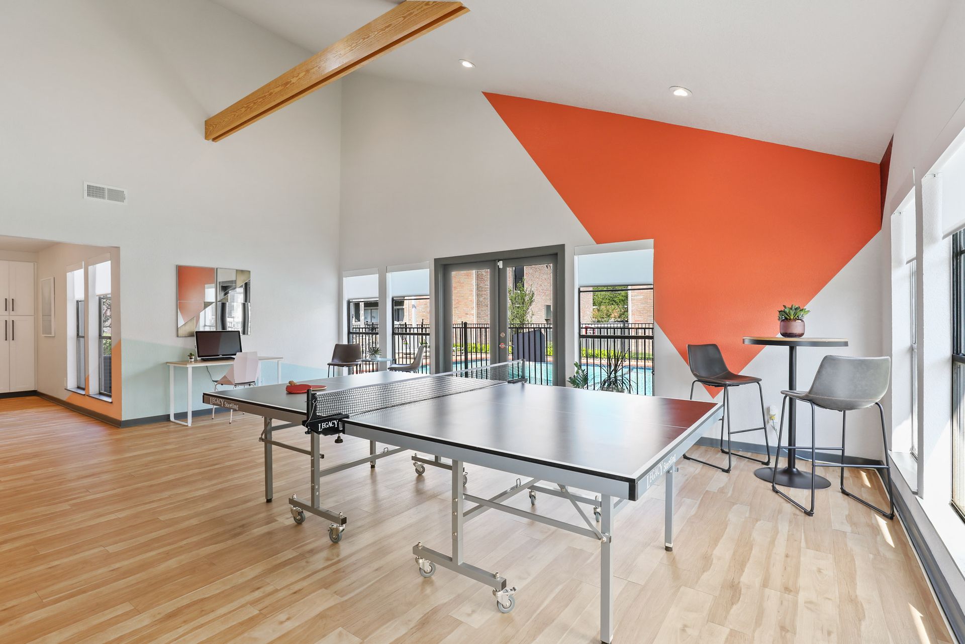 A modern rec room with ping pong table, orange accent wall, and light wood flooring.