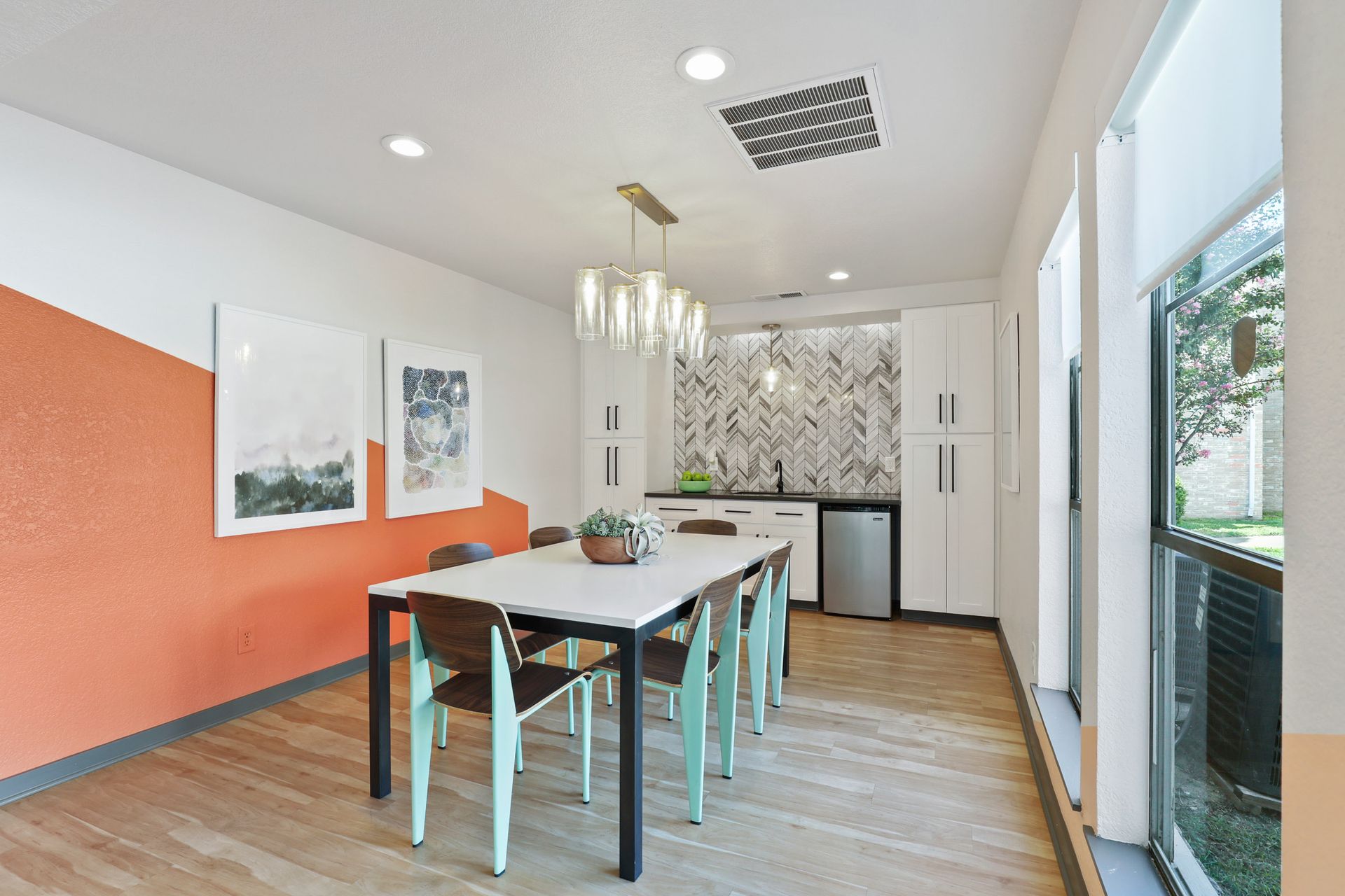Dining area with a table and chairs, orange and white walls, and a small kitchenette.