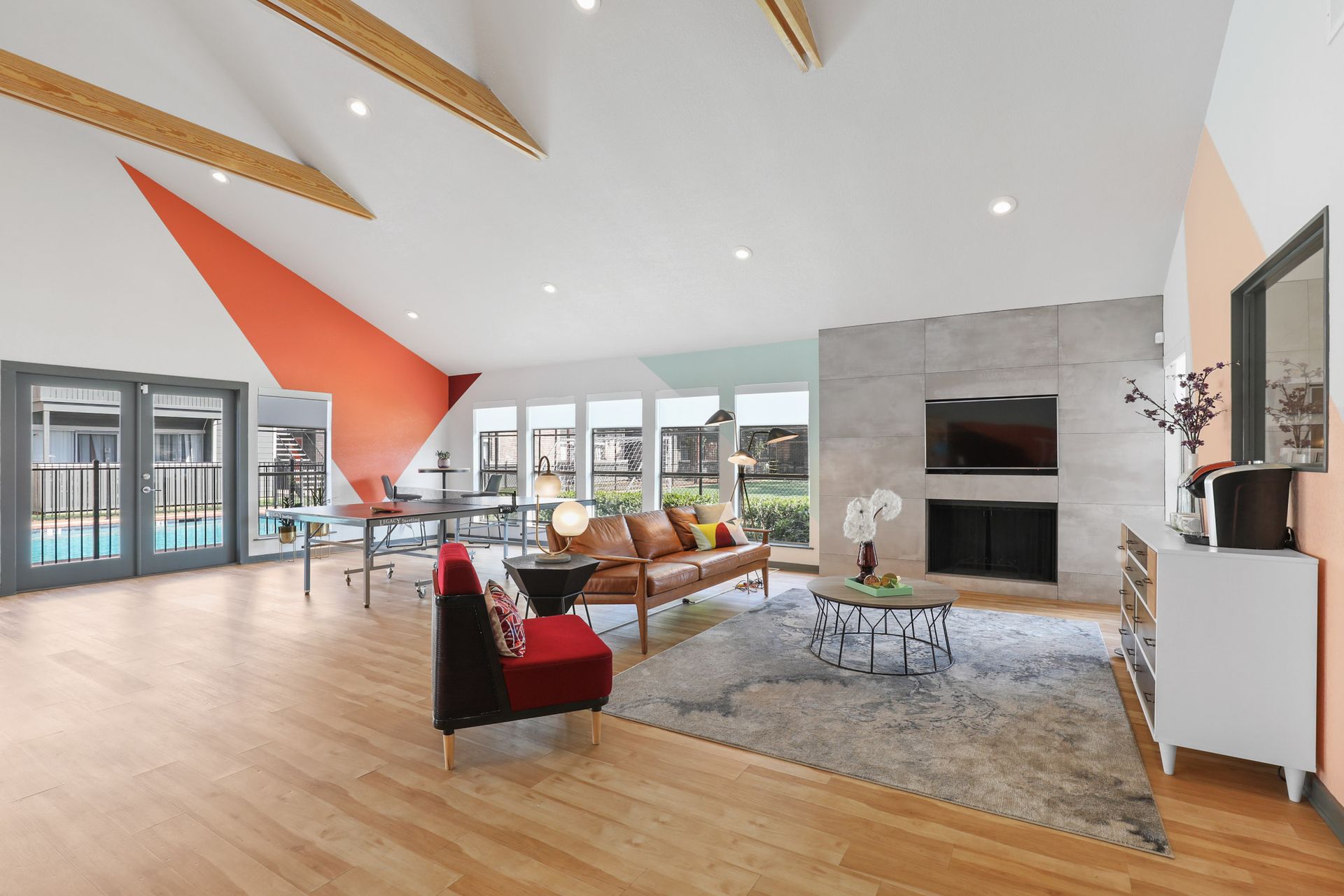 Open-concept living room with a pool view, featuring a fireplace, modern furniture, and an orange accent wall.