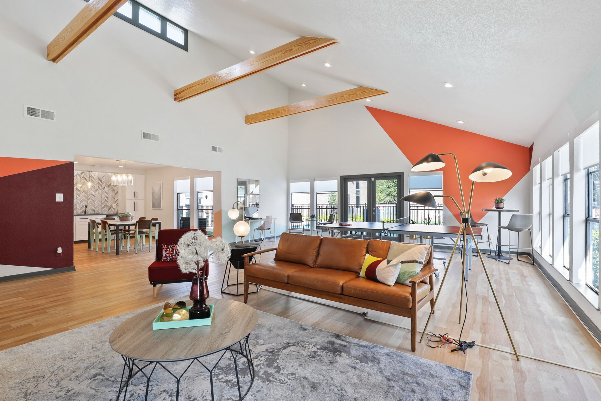 Open-plan living space with high ceilings, exposed beams, and a brown leather sofa. Features orange and burgundy accent walls.
