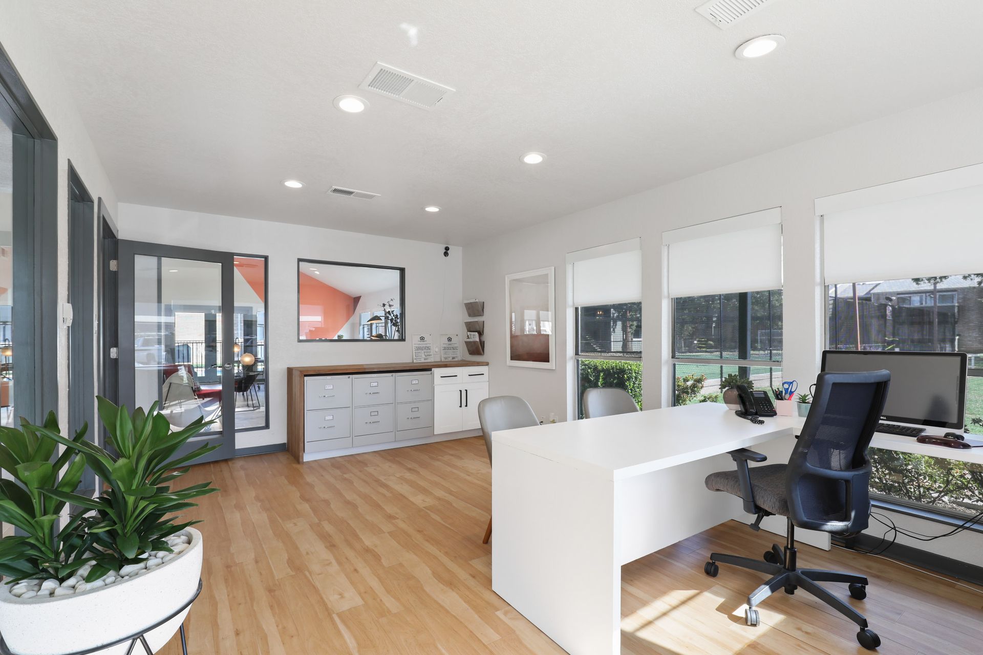 Modern office with white desk, chair, cabinets, and large windows overlooking a lawn.