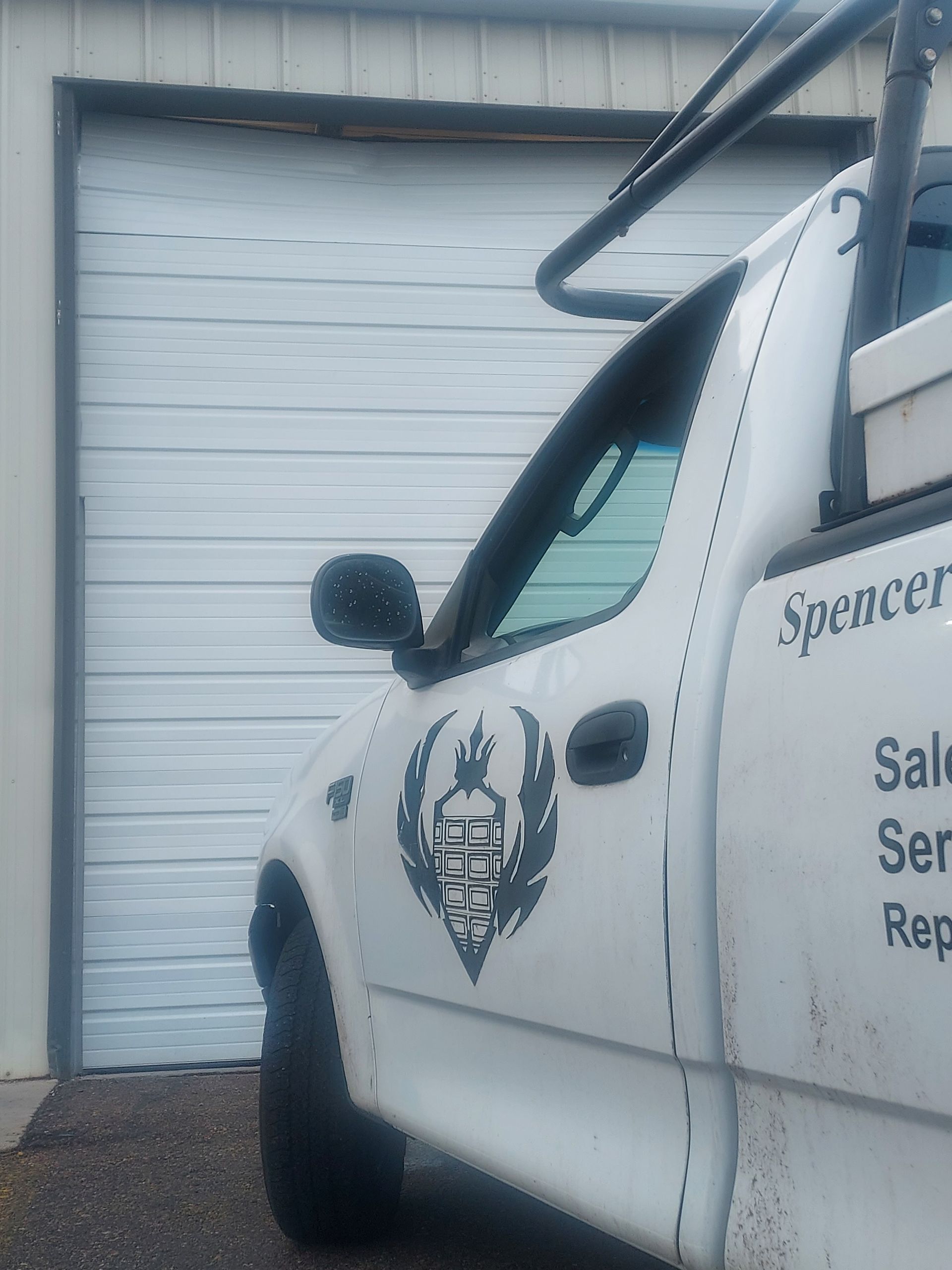 A close-up of a white utility truck with a skull logo on the door, parked in front of a white garage door.