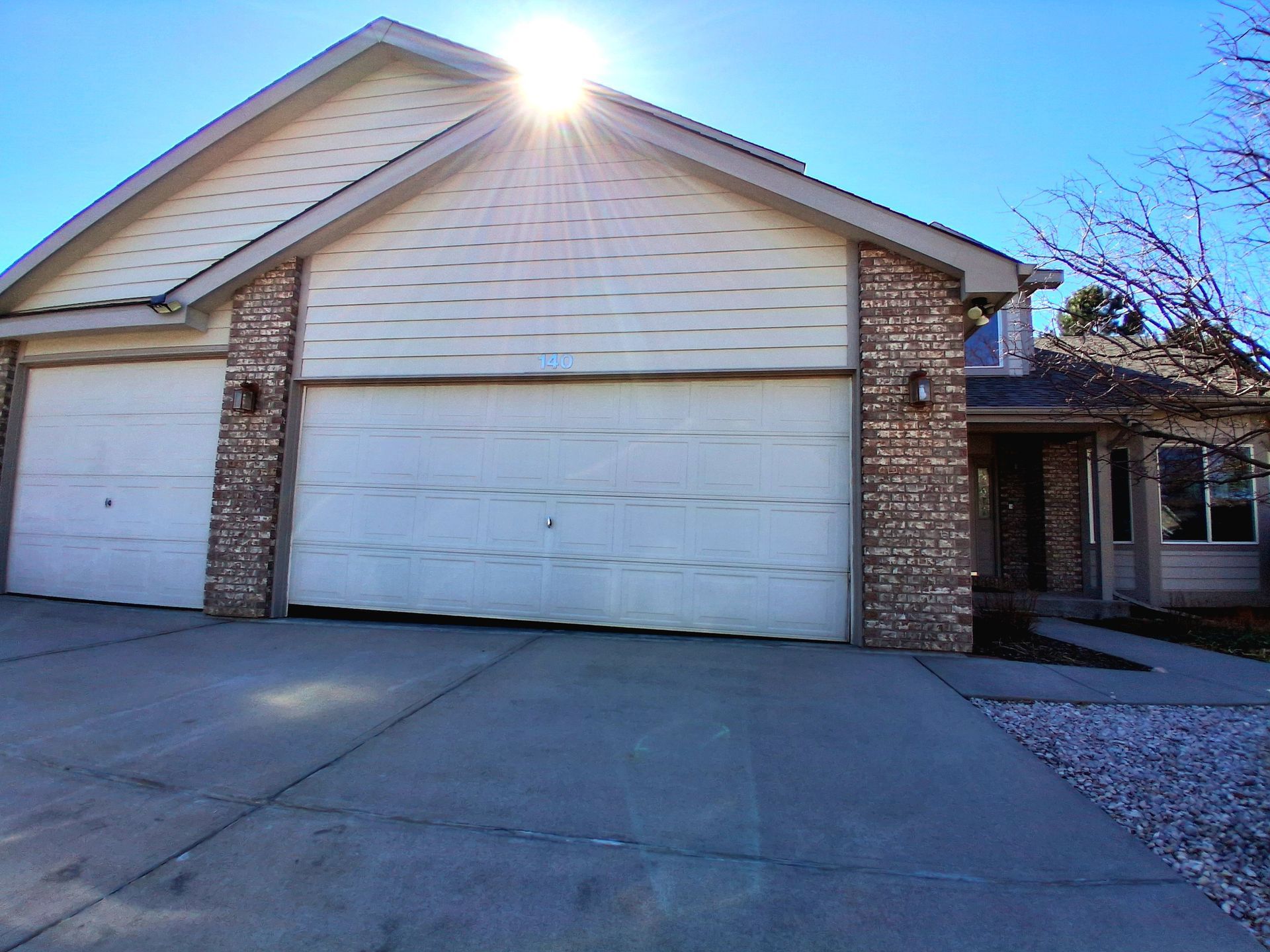 A beige house exterior with a multi-car garage, brick accents, and a concrete driveway on a sunny day.