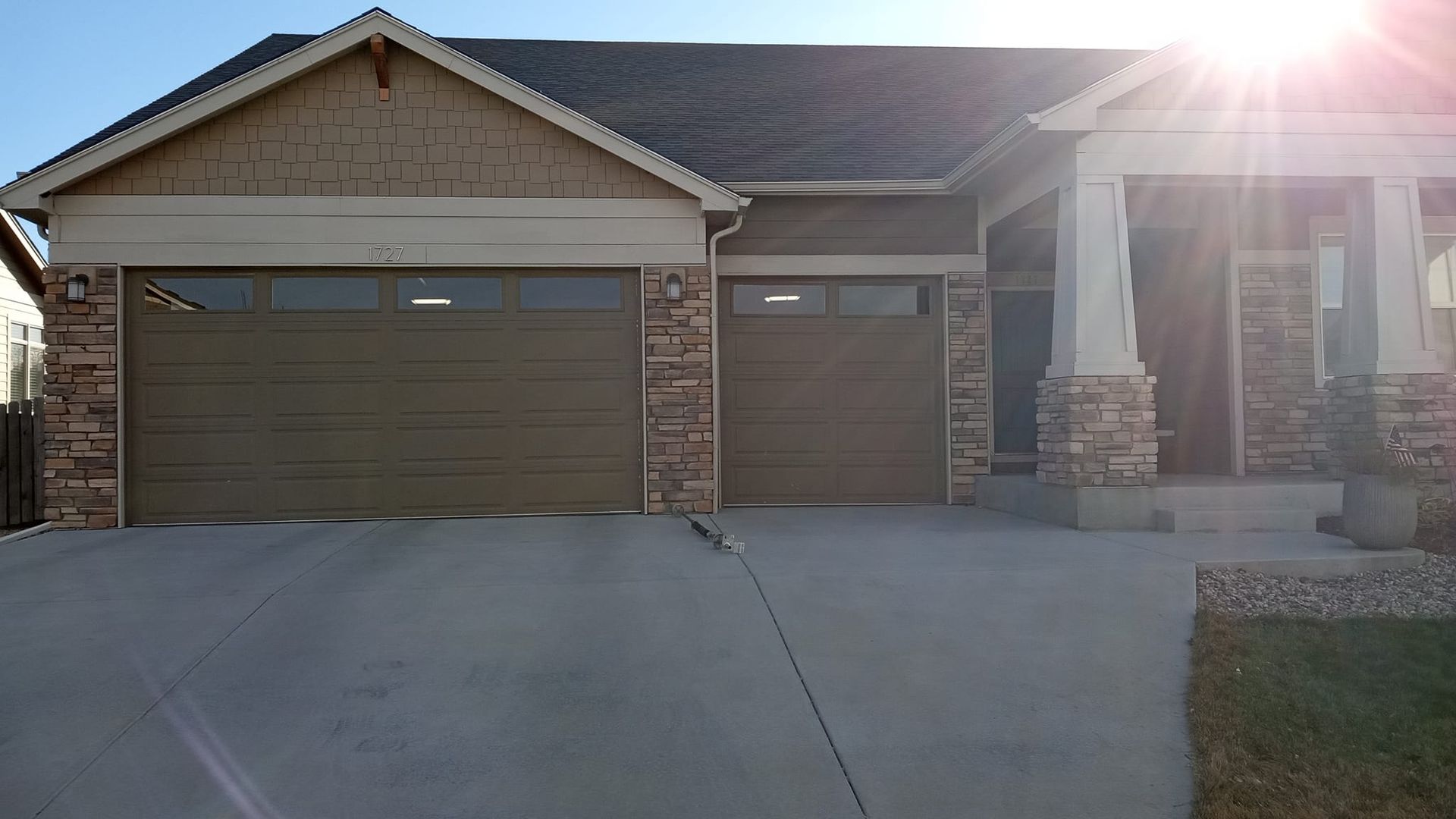 A modern single-story suburban house with a two-car garage, stone facade, and a concrete driveway on a sunny day.