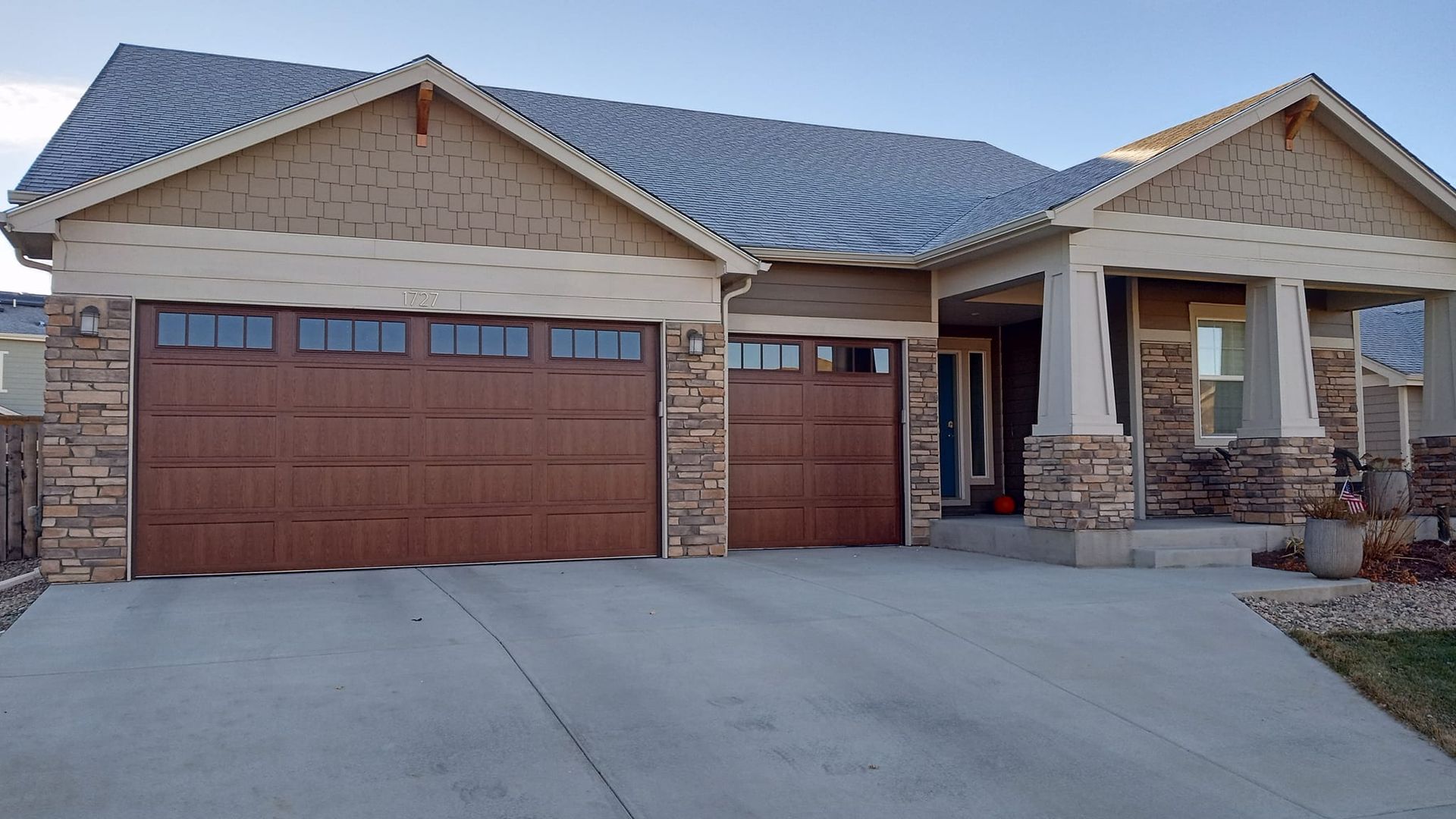 A single-story suburban home with a two-car garage, stone facade, light tan siding, and a covered front porch.