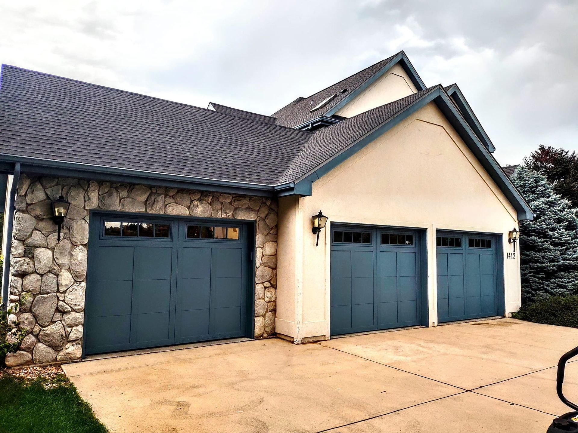 A house exterior with three dark blue garage doors, a stone facade on the left, and cream-colored stucco on the right.