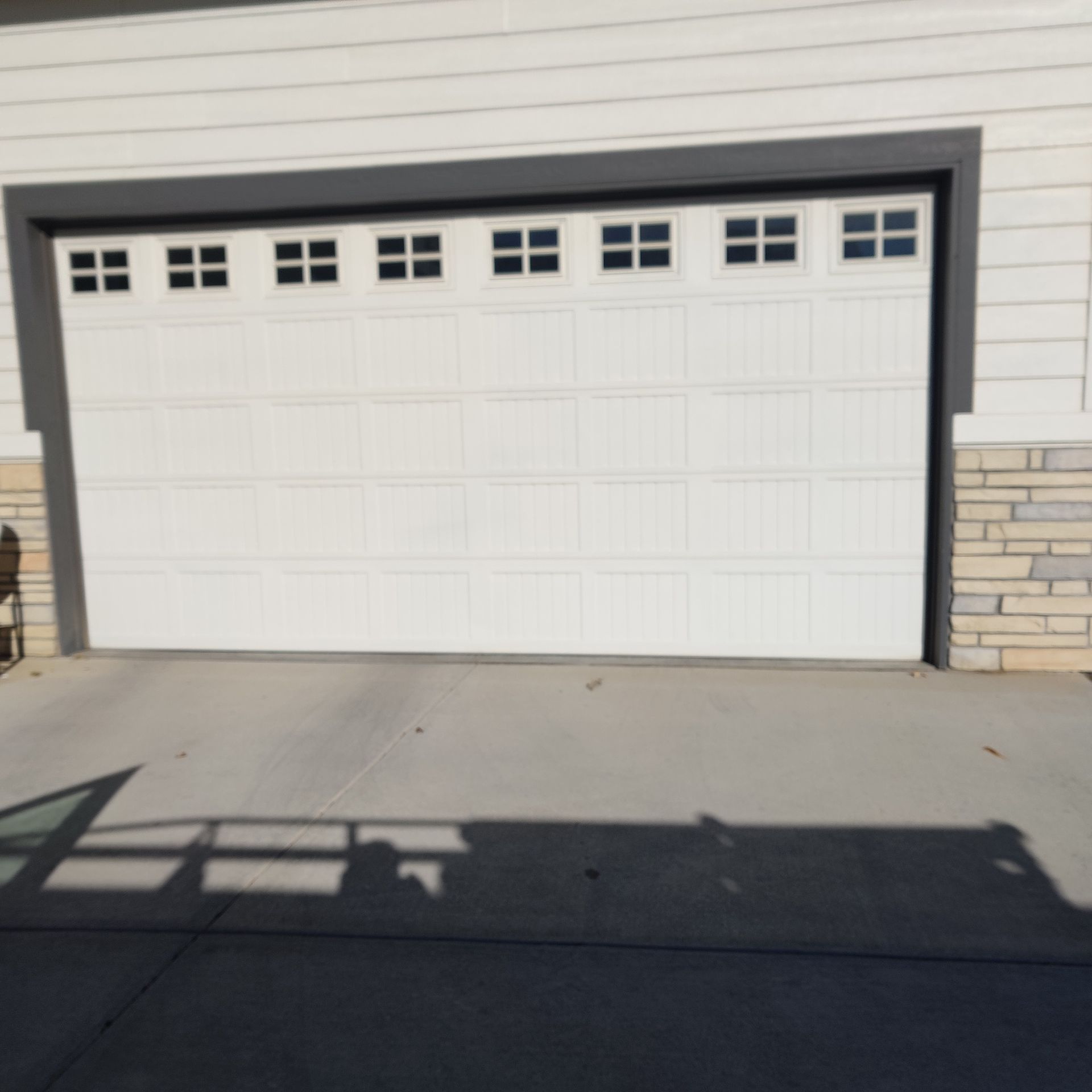 White garage door with windows, surrounded by beige horizontal siding and light-colored stone veneer.