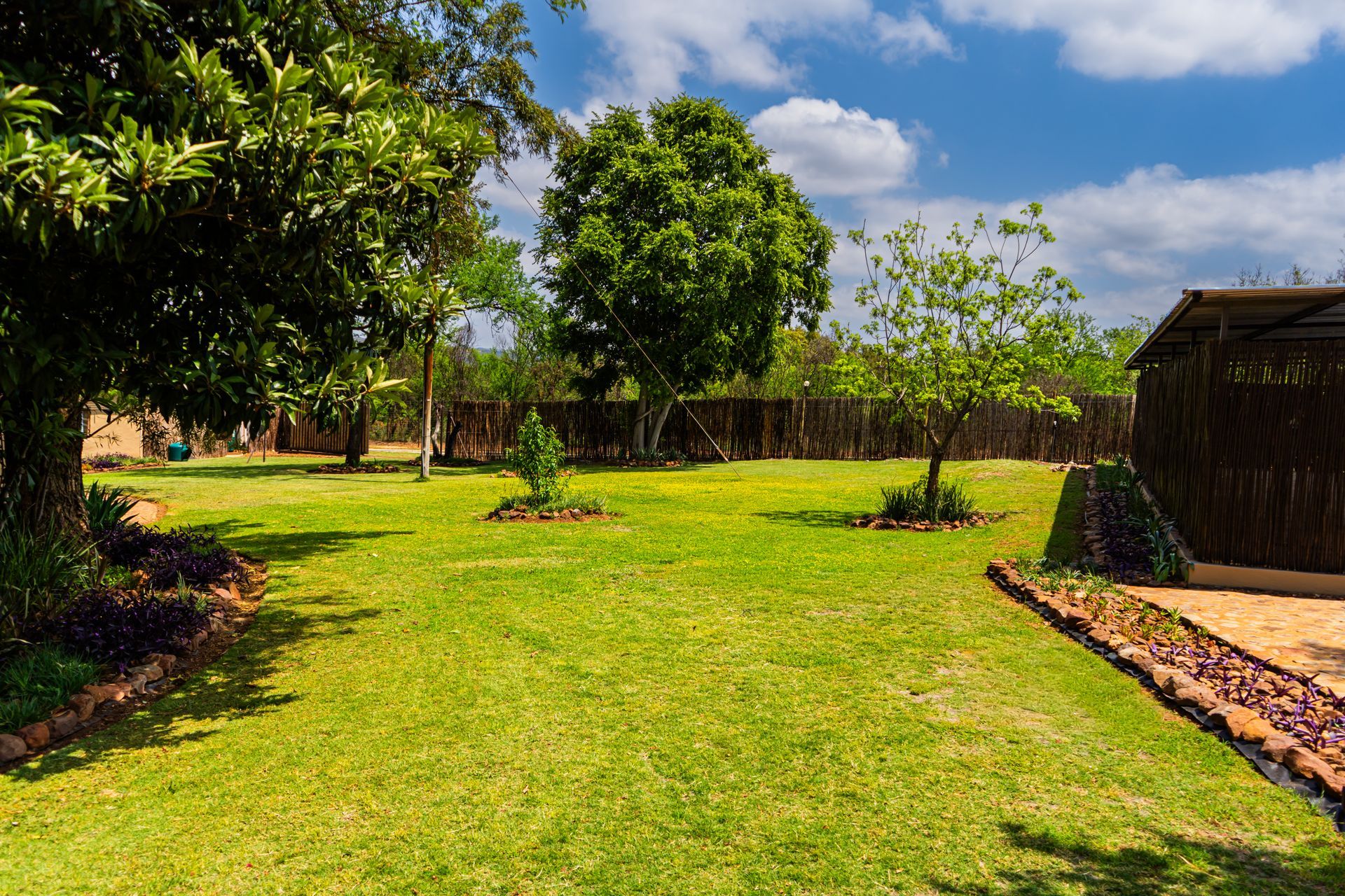 Tranquil garden at El-Tsuri Guest Resort in Hartbeespoort, featuring lush green lawns, flowering plants, shaded seating areas, and mountain views — a peaceful retreat surrounded by nature.