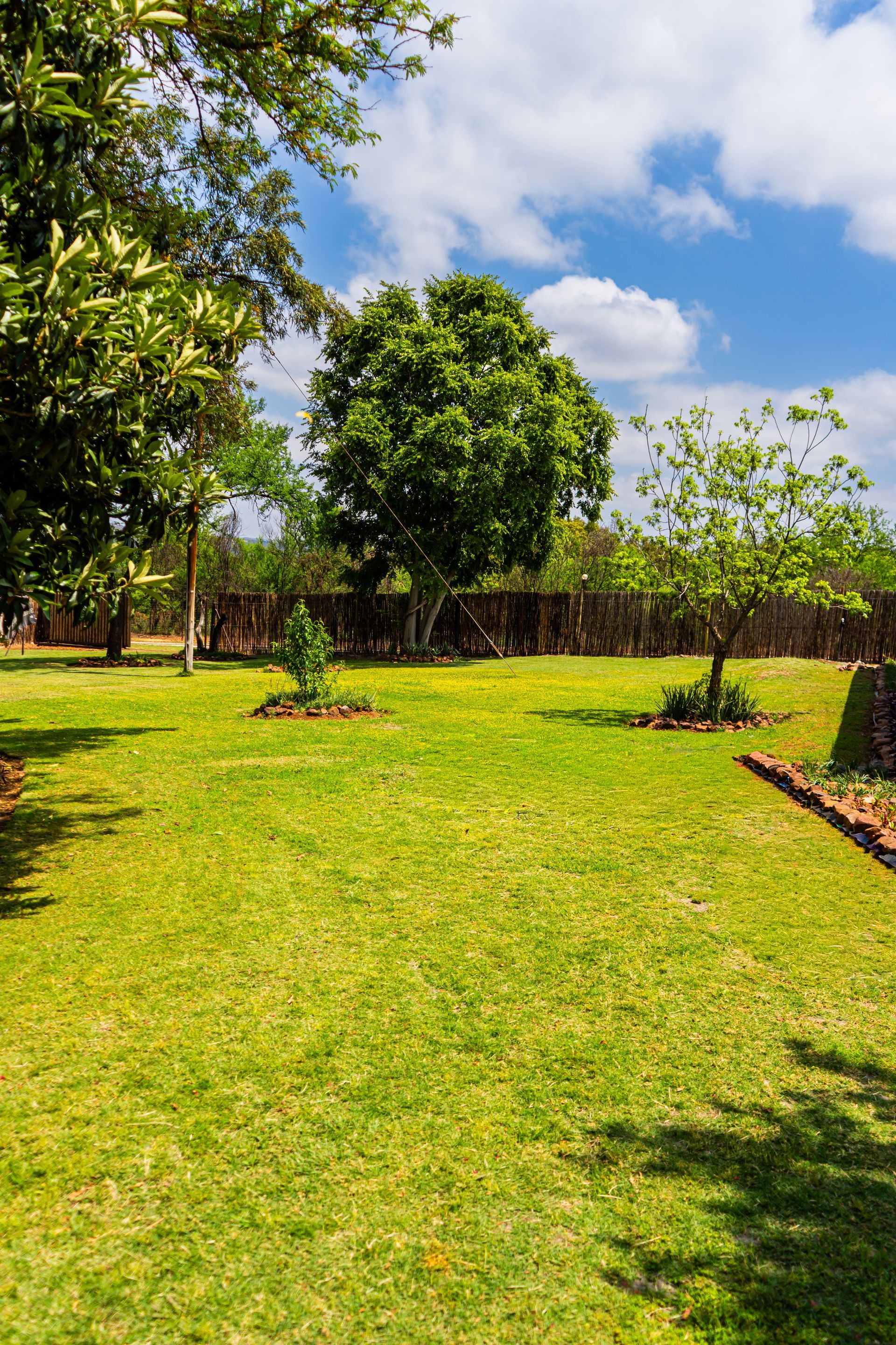 Beautiful landscaped garden at El-Tsuri Guest Resort in Hartbeespoort, with vibrant flowers, tall trees, and cozy gazebos creating a serene atmosphere for relaxation and outdoor enjoyment.