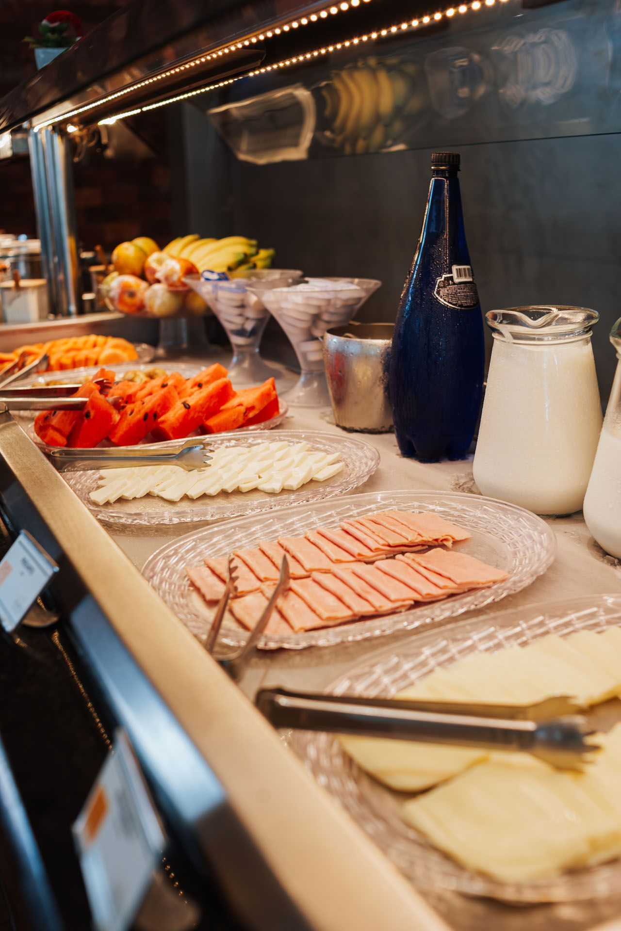Buffet com tomates, queijo, presunto e jarras de leite. Uma garrafa azul também está disponível no buffet.