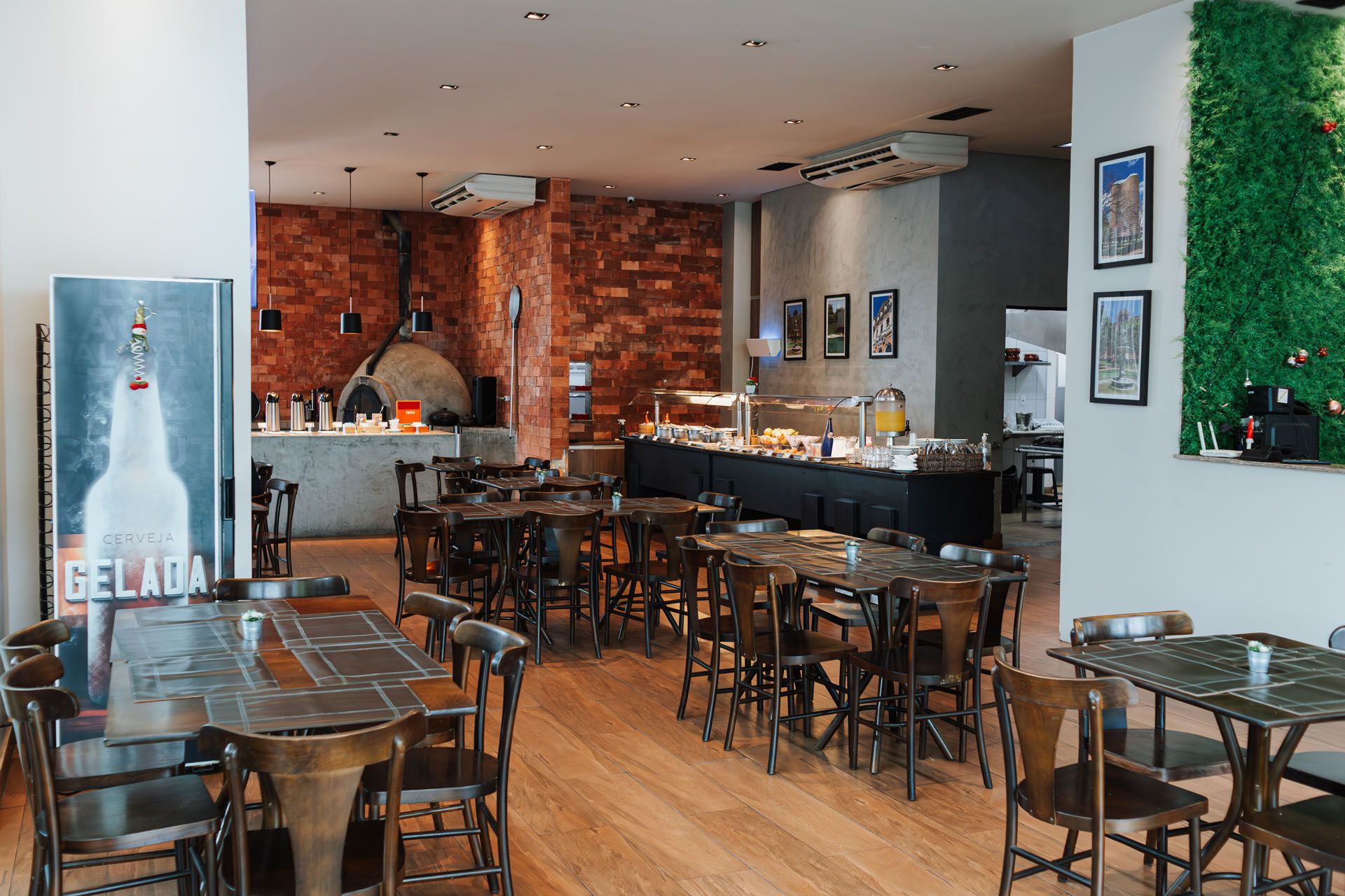 Interior de restaurante com mesas, cadeiras, parede de tijolos, forno de pizza e bufê.