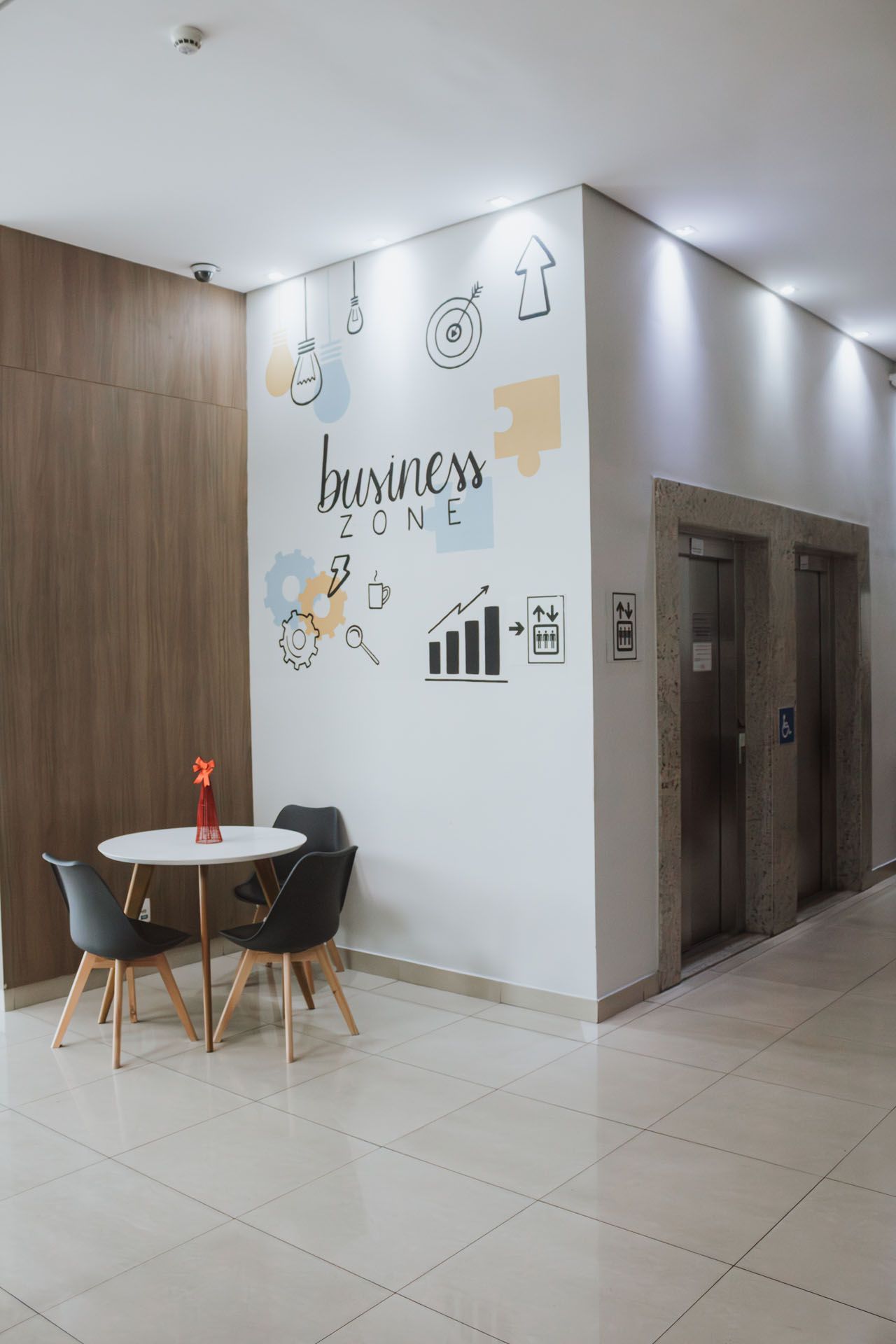 Hall de entrada moderno com uma pequena mesa e cadeiras, arte de parede com a inscrição "zona de negócios" e elevadores.