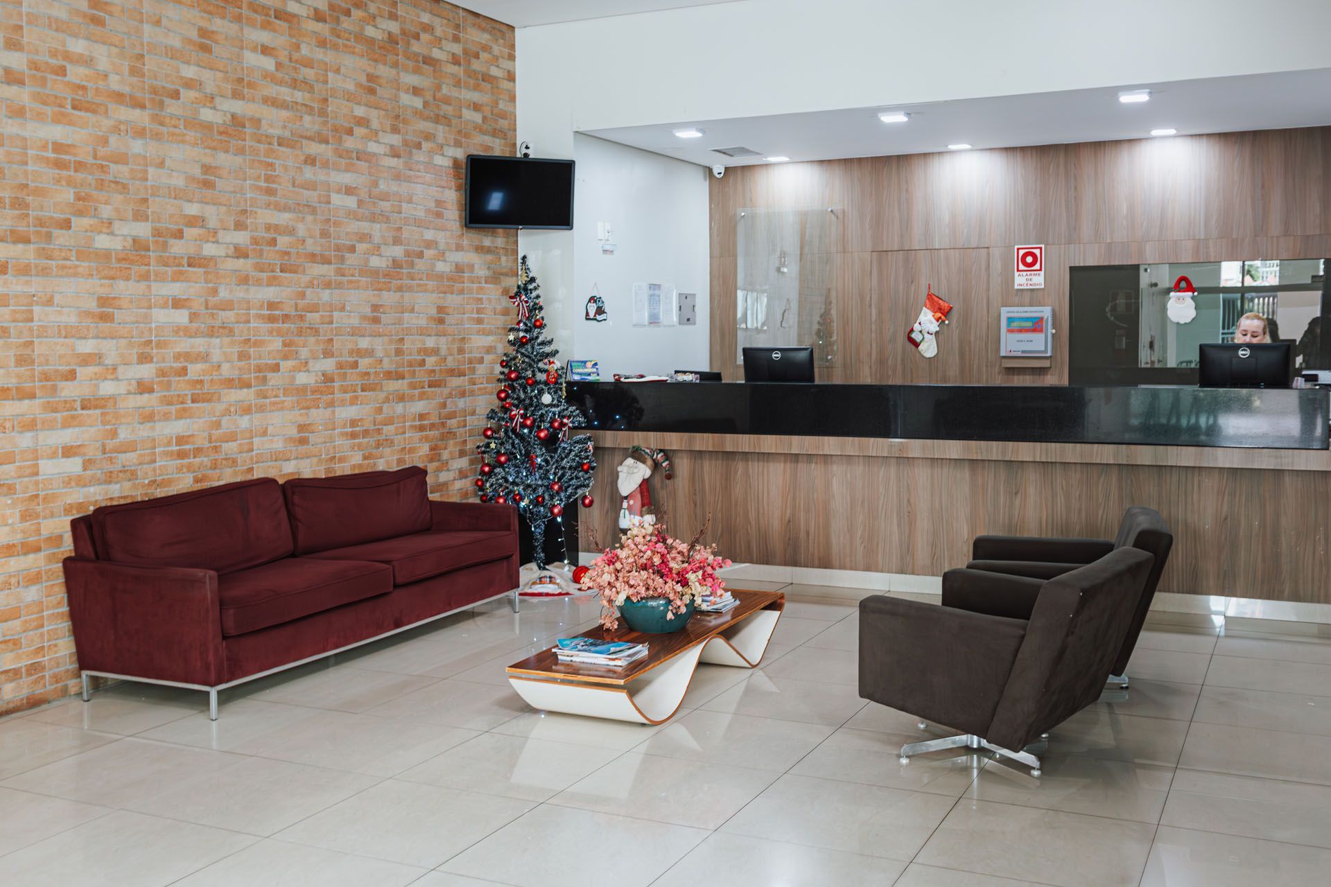 Hall de entrada do hotel com parede de tijolos, sofá, cadeiras, balcão de recepção e decoração natalina.