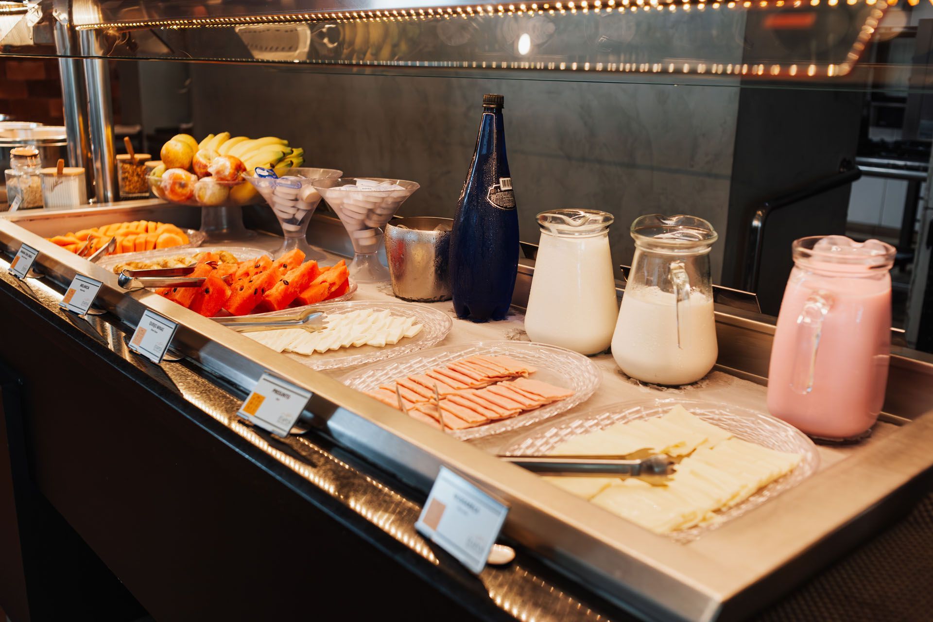 Buffet de café da manhã com frutas, iogurte, queijo e presunto.