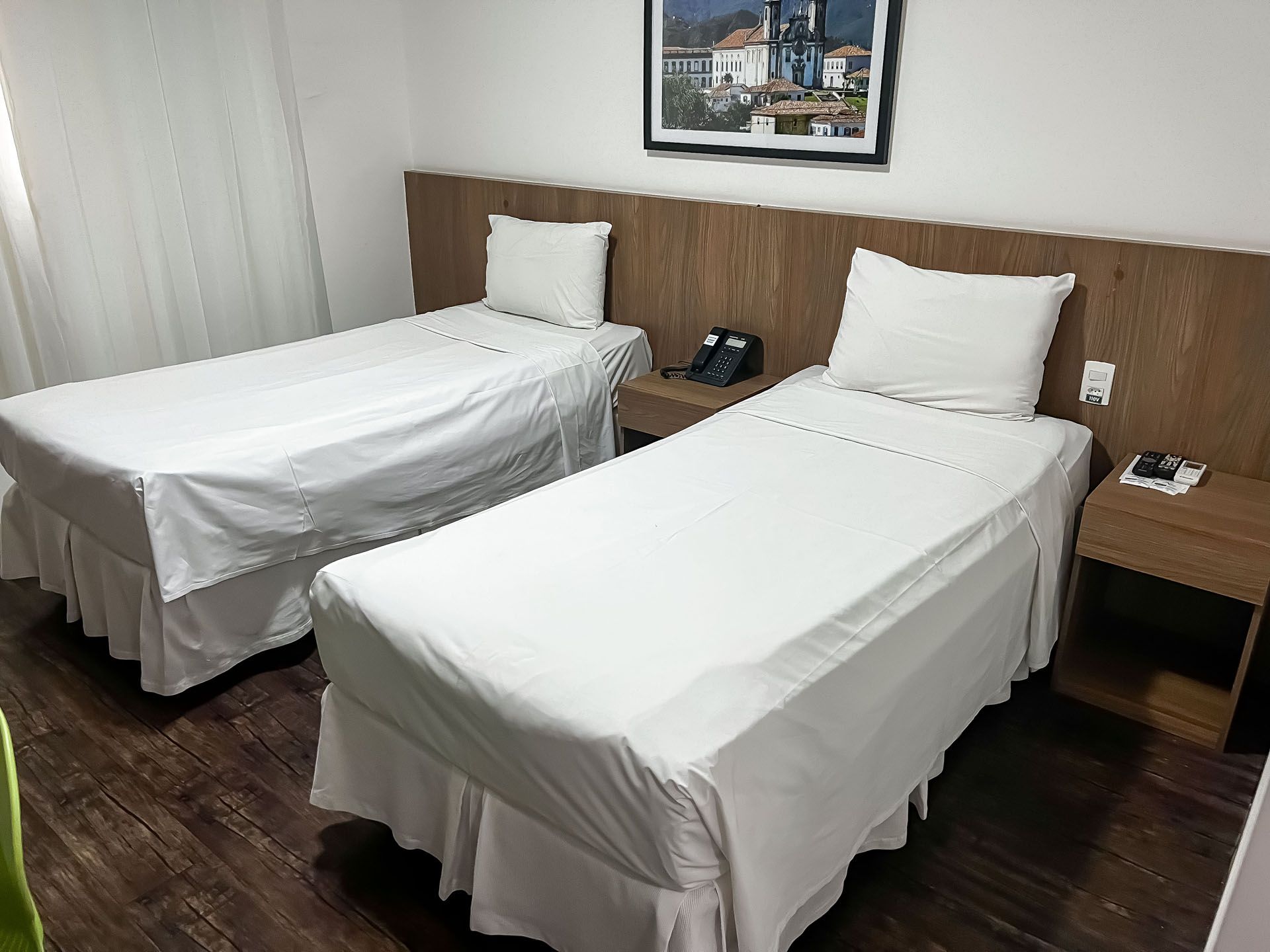 Duas camas de solteiro com lençóis brancos em um quarto de hotel, com uma mesa de cabeceira entre elas.