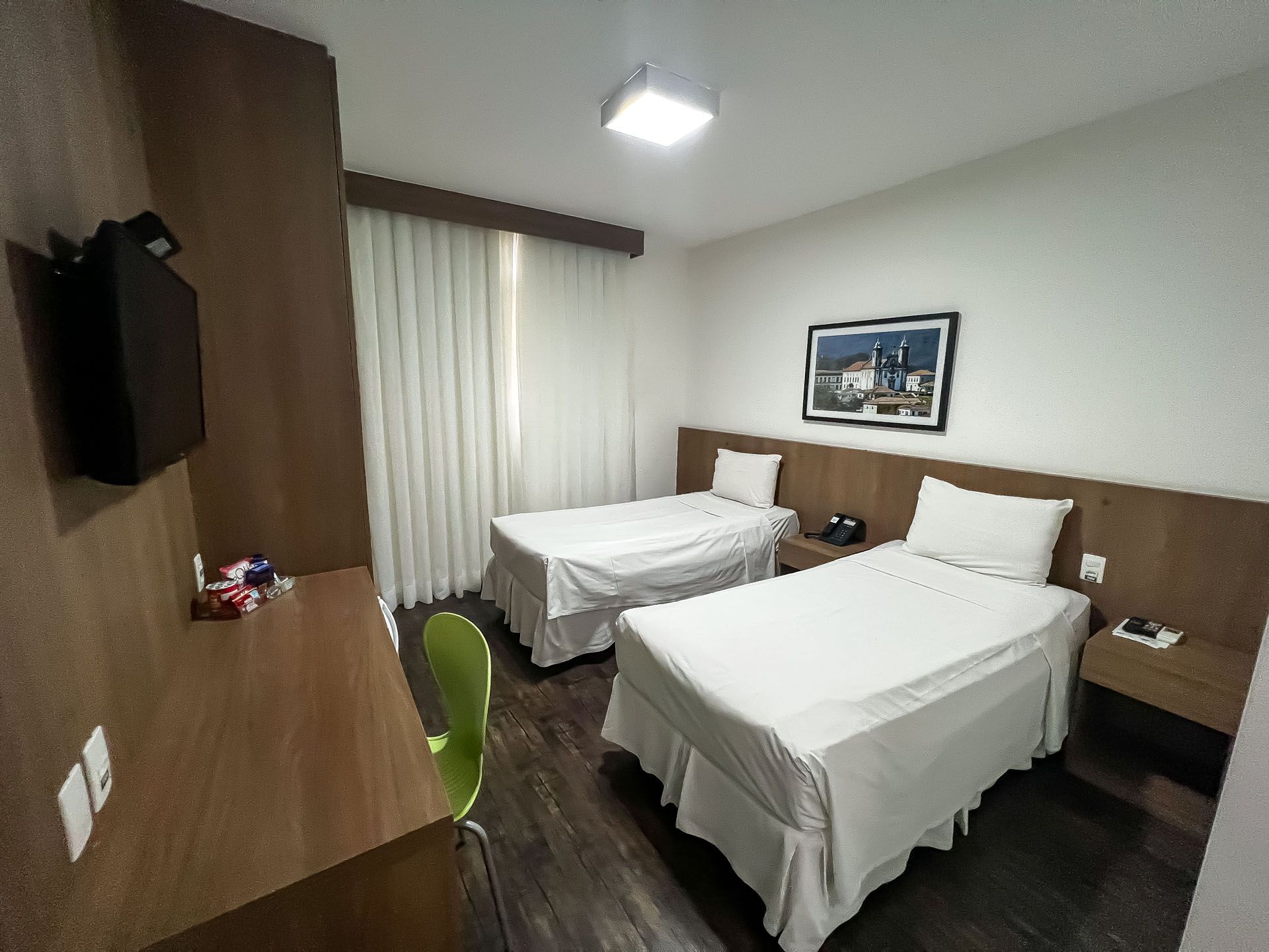 Quarto de hotel com duas camas, escrivaninha, TV e obras de arte na parede.
