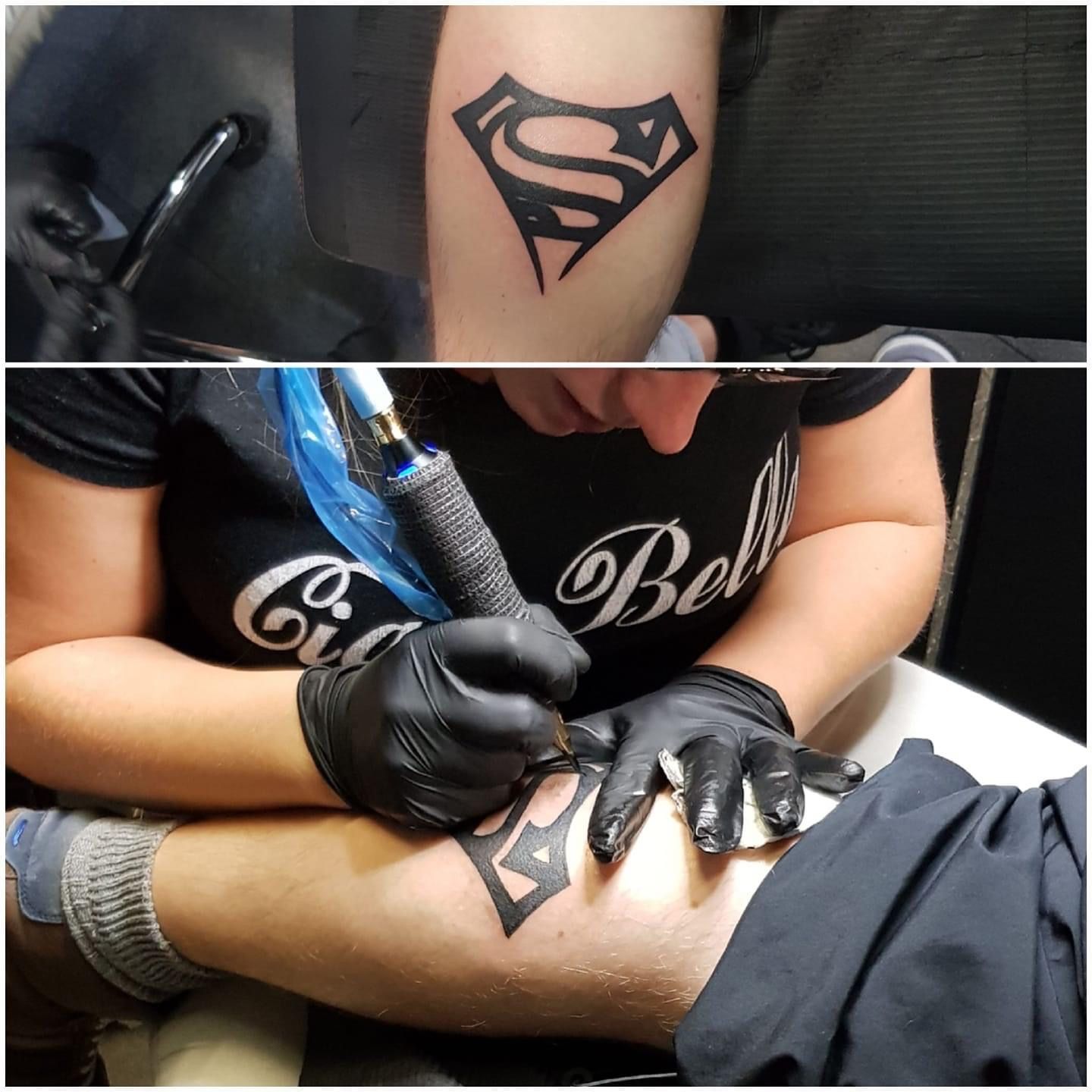 Tatoeëerder met zwarte handschoenen die een zwart Superman-symbool op een been tatoeëert. Bovenste afbeelding: tatoeage op arm.