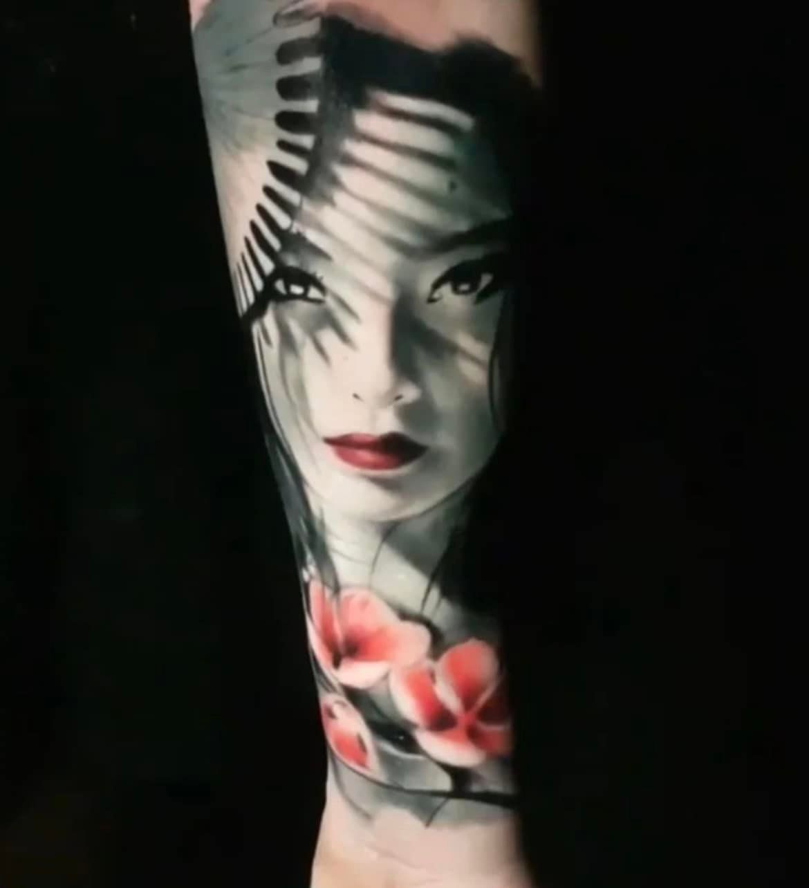 Tatoeage van een vrouwengezicht, gearceerd, met rode lippen en bloemen op de arm; schaduwen van palmbladeren op het gezicht.