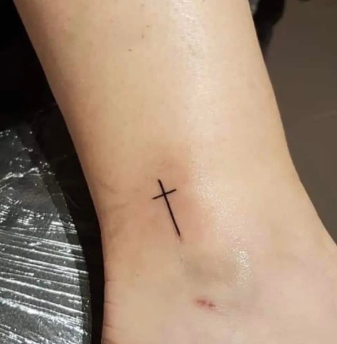 Kleine, minimalistische kruis-tatoeage op een enkel.
