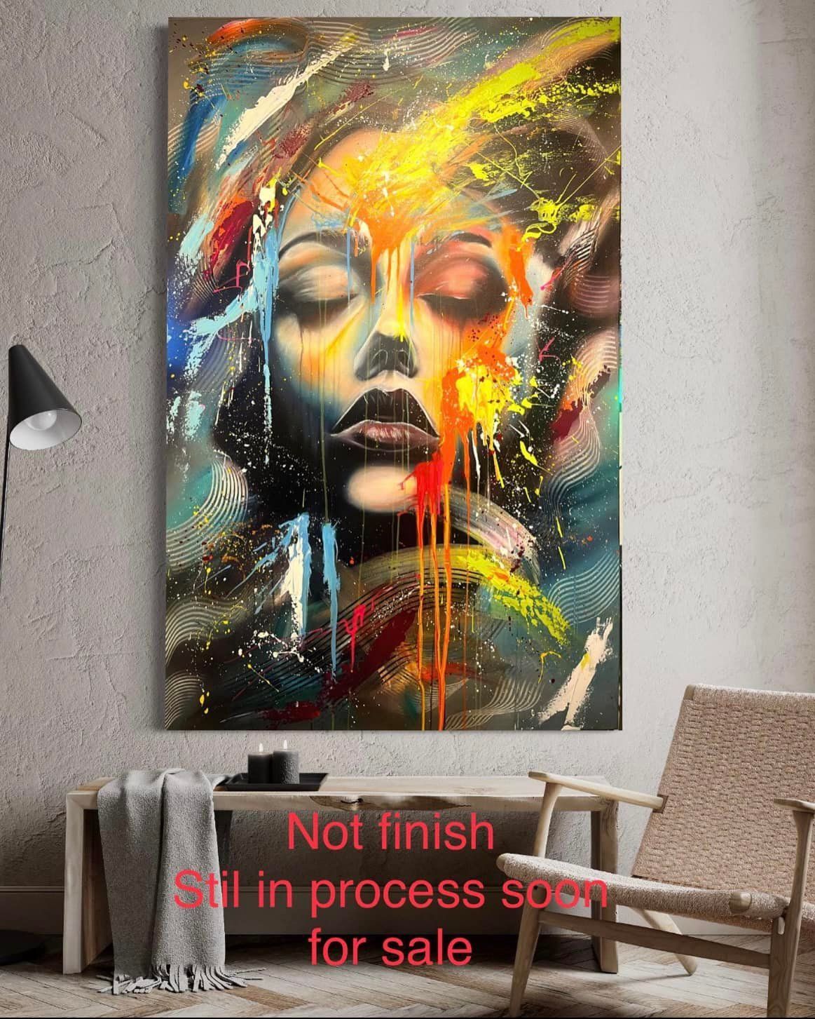 Abstract schilderij van een vrouwengezicht met gesloten ogen, levendige verfspatten. Het hangt aan een muur boven een tafeltje.