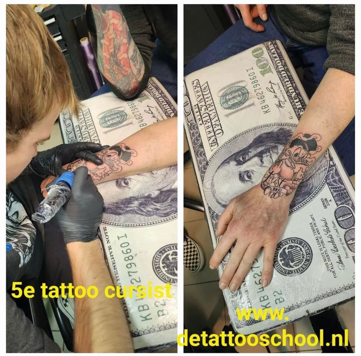 Tatoeëerder tatoeëert een onderarm op een ondergrond met een geldthema. Close-up van de tatoeage in uitvoering, een voltooide tatoeage is zichtbaar.