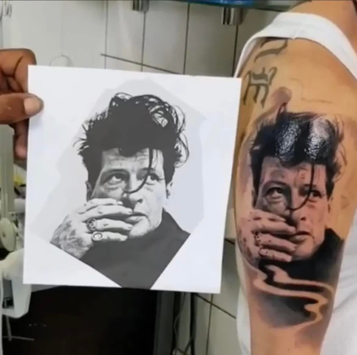 Tatoeage van een persoon die zijn mond bedekt, vergeleken met de foto. Zwarte inkt, op een schouder, in een tattoostudio.